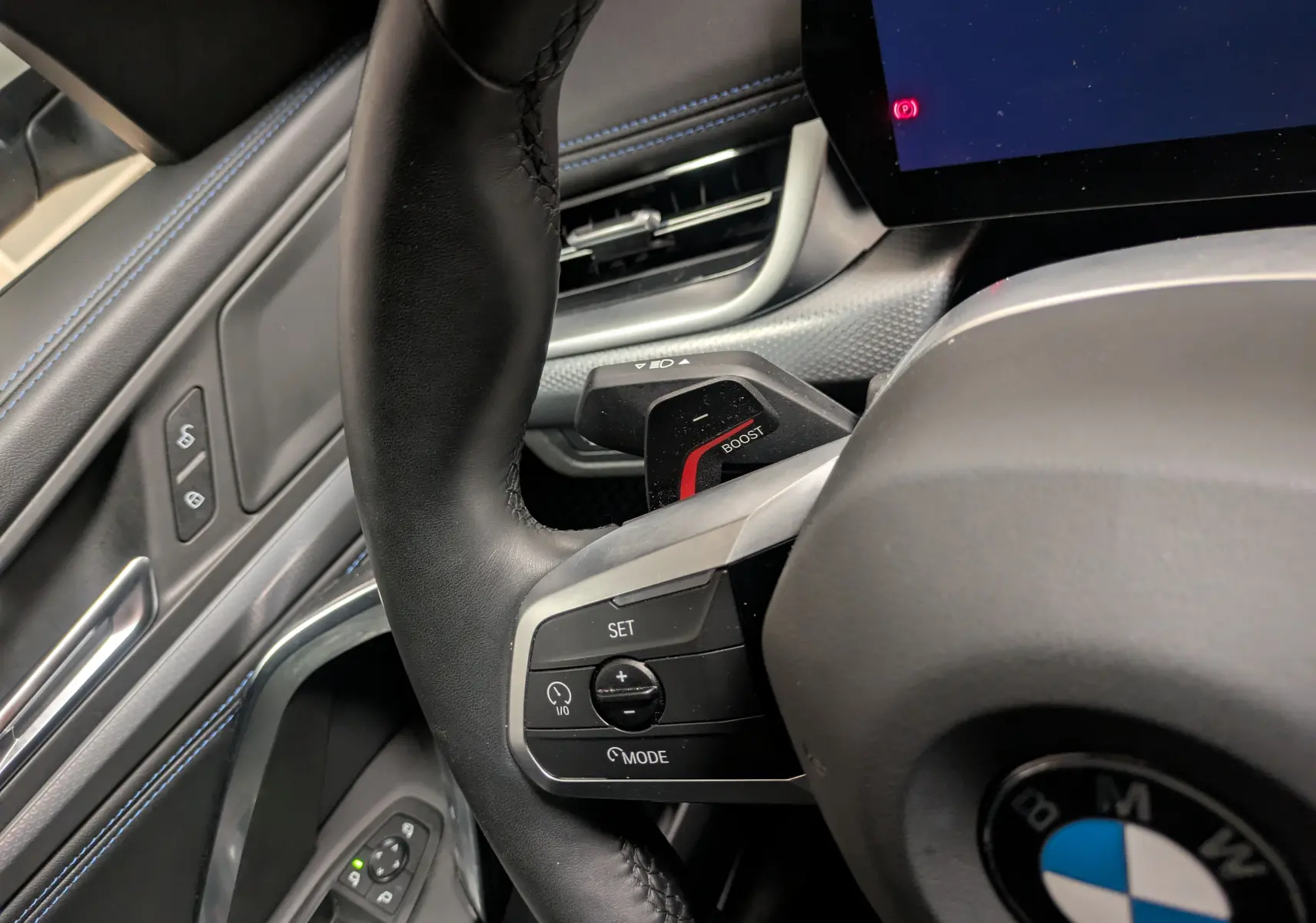 Gros plan intérieur sur le volant cuir M noir avec commandes multifonctions et détails bleus sur la portière côté gauche.