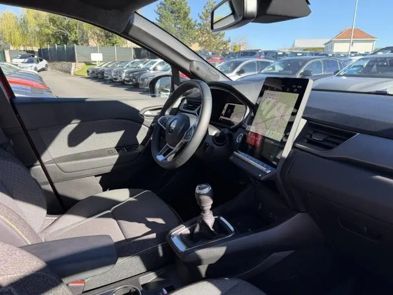 Intérieur du Renault Captur 2025 rouge, vue côté conducteur montrant le volant, la boîte manuelle et l'écran tactile central.