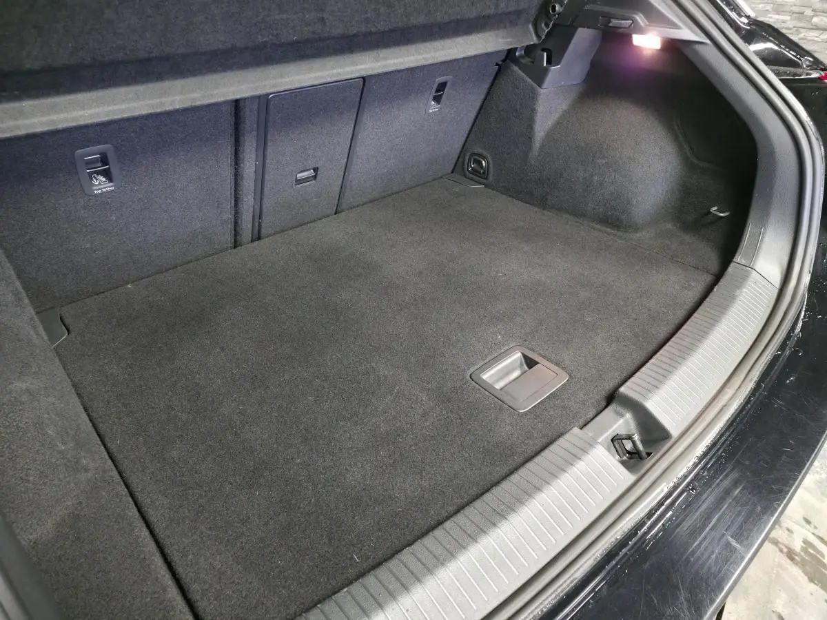 Vue intérieure du coffre spacieux et propre du Volkswagen T-Roc noir, avec éclairage latéral et revêtement en tissu gris foncé.