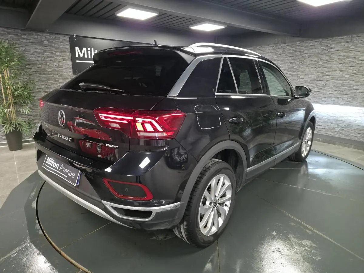 Volkswagen T-Roc noir vue 3/4 arrière droit en intérieur avec feux arrière LED allumés et jantes alliage.