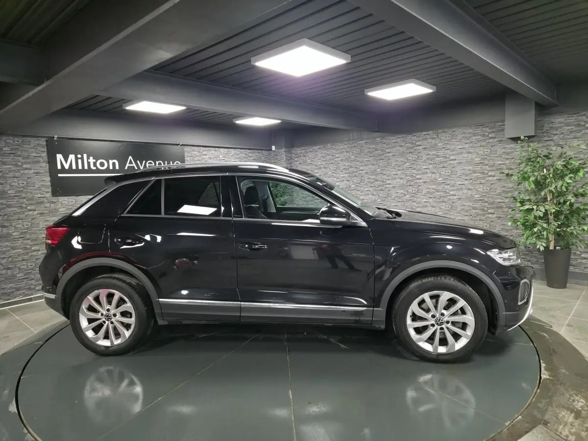 Volkswagen T-Roc noir en profil droit dans un showroom avec jantes alliage 17 pouces et vitres surteintées.
