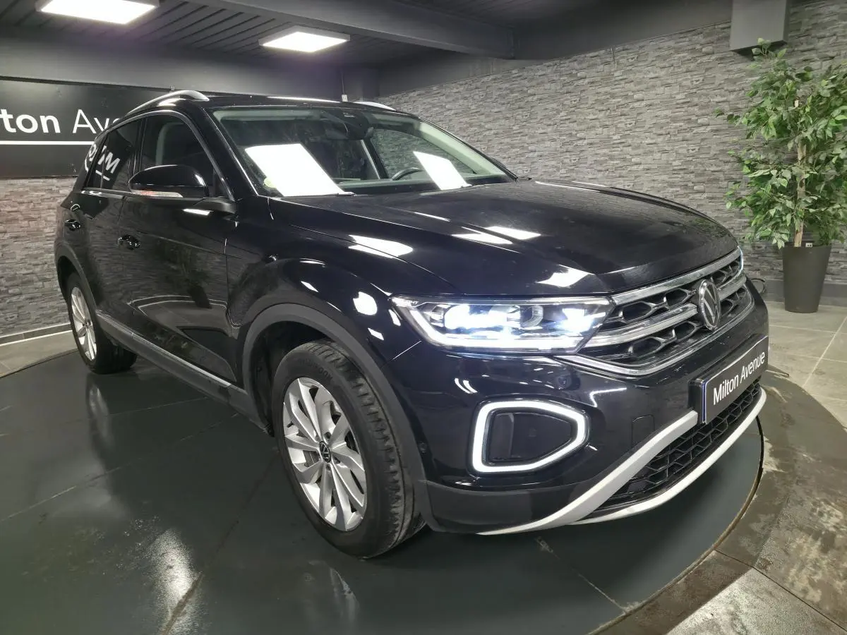 Volkswagen T-Roc noir métallisé vu en 3/4 avant droit avec phares LED allumés en showroom.
