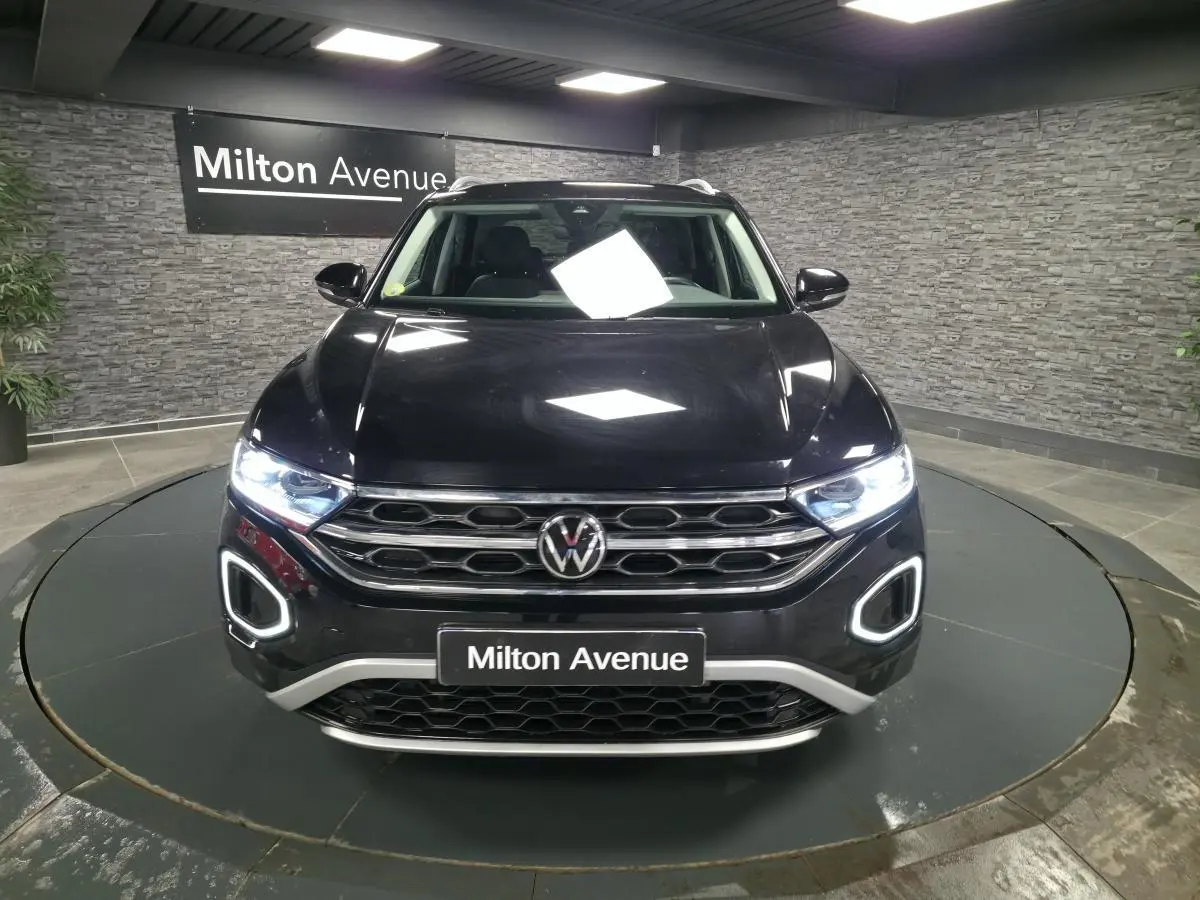 Volkswagen T-Roc noir vu de face, avec feux LED allumés et calandre chromée dans un showroom.