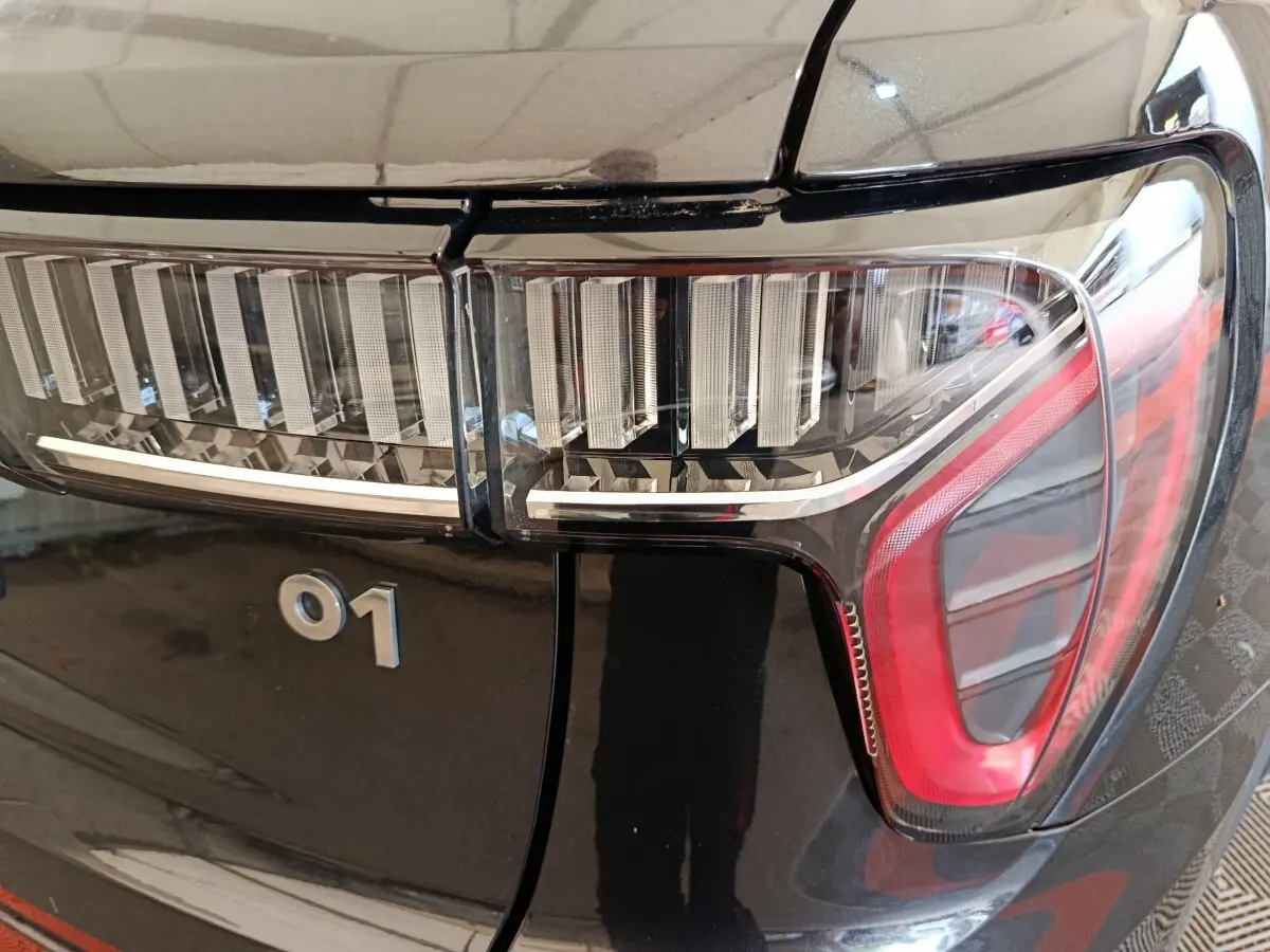 Gros plan sur le feu arrière droit noir brillant du LINK & CO 01 avec logo 01 visible sur la carrosserie.