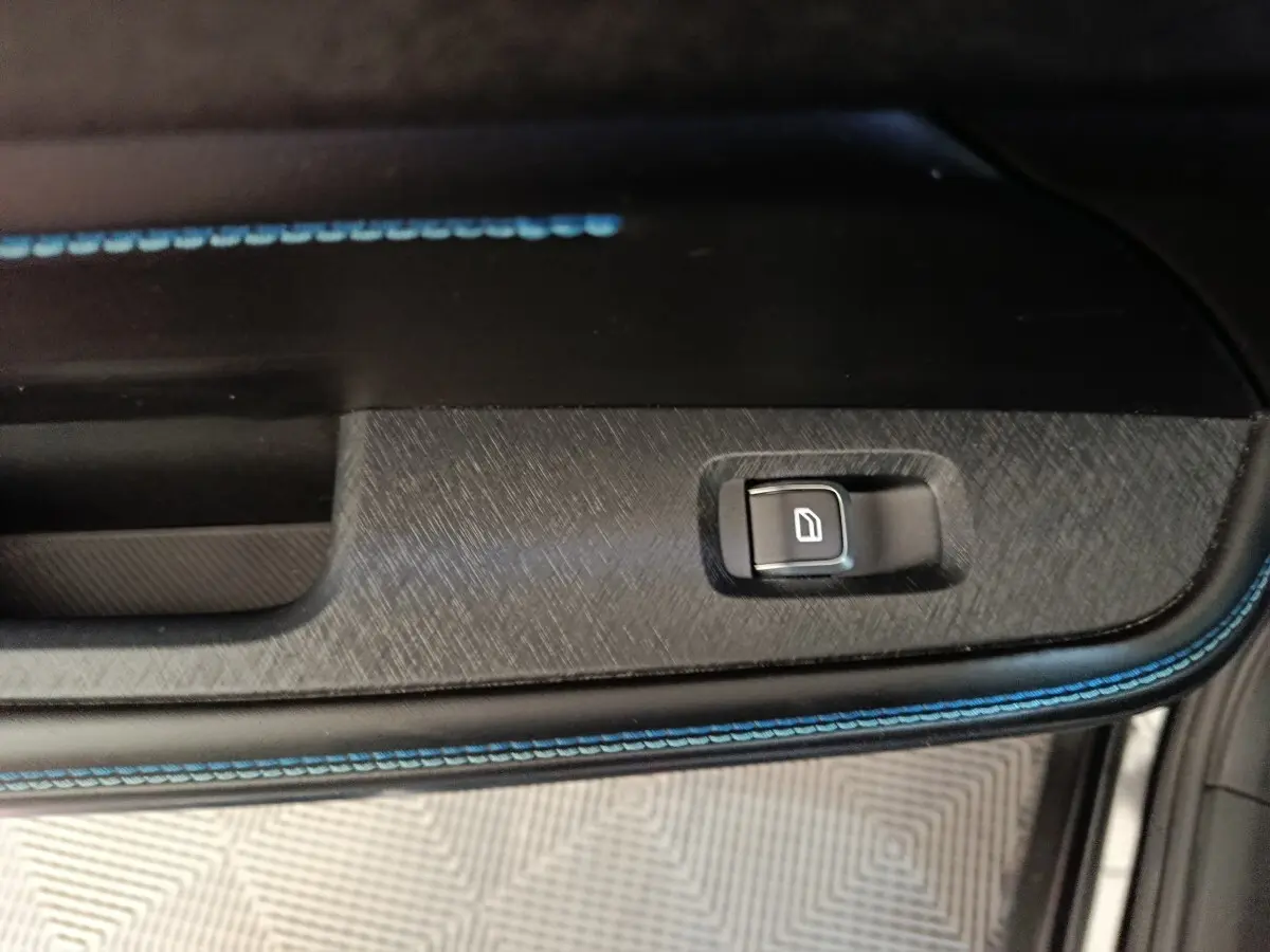 Gros plan sur la commande de lève-vitre côté porte intérieure avec surpiqûres bleues sur garniture noire.