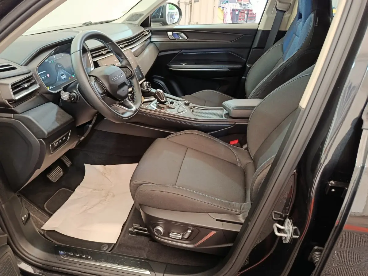 Vue intérieure côté conducteur du SUV noir Link & Co 01 2023, avec tableau de bord digital et sièges tissu gris.