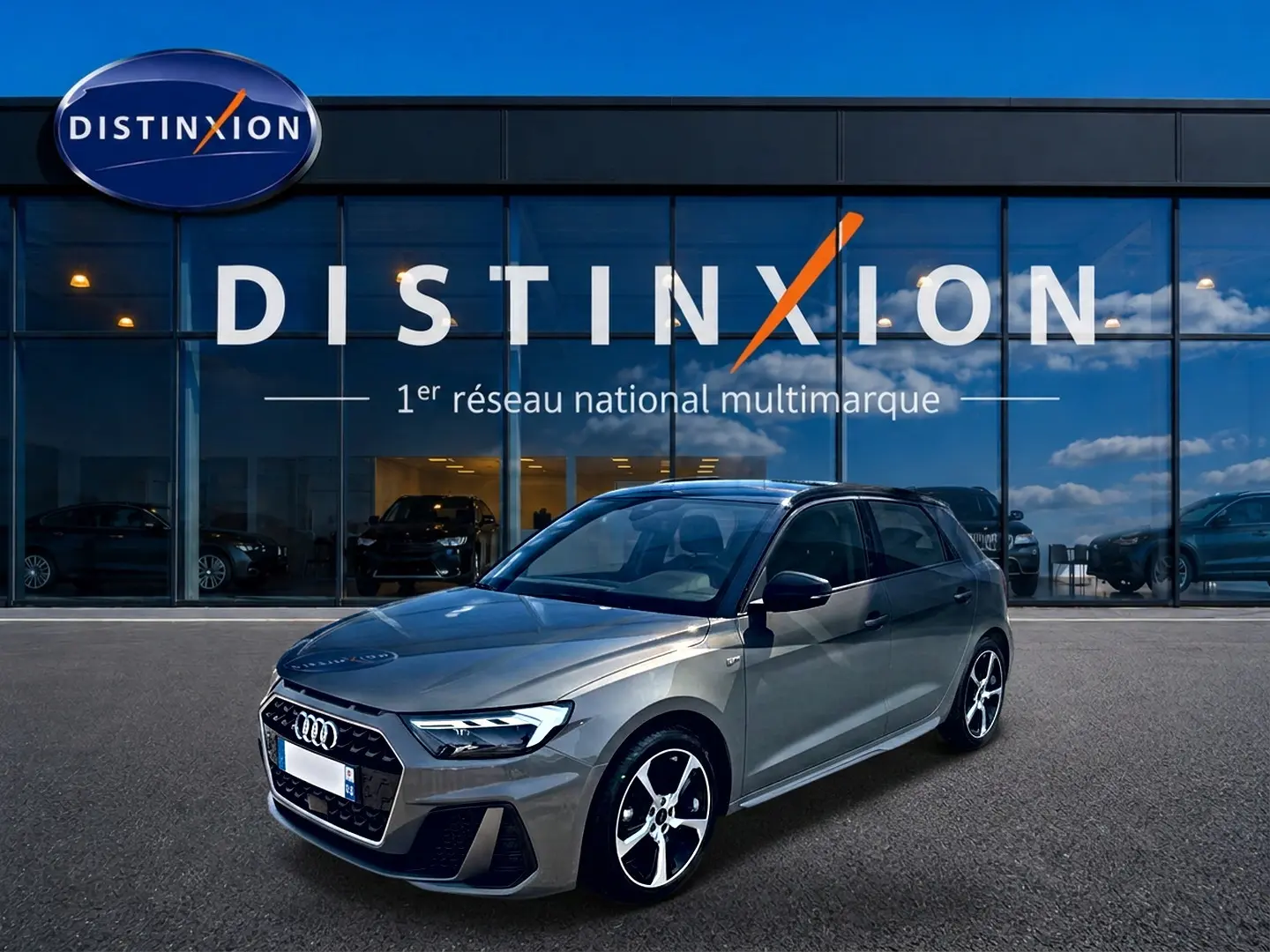 Audi A1 Sportback gris chronos vue 3/4 avant droit devant une vitrine Distinxion, jantes alu et toit noir.