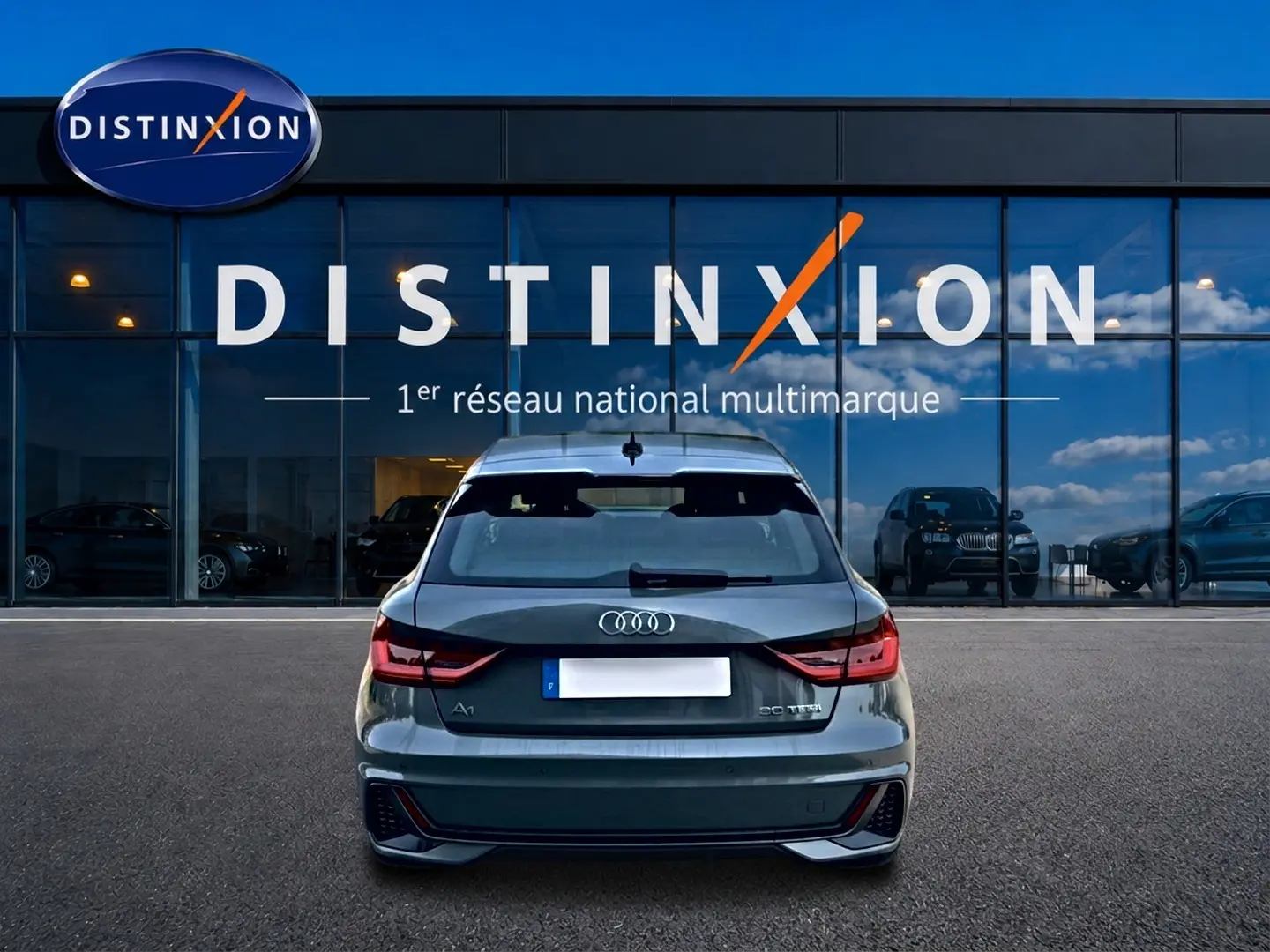 Vue arrière d'une Audi A1 Sportback gris chronos avec feux LED et becquet arrière, stationnée devant une vitrine Distinxion.