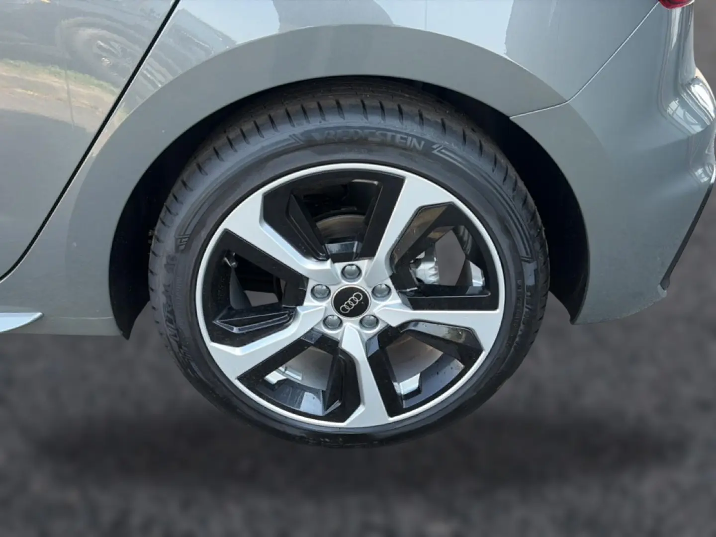 Gros plan sur la roue arrière droite de l'Audi A1 Sportback gris chronos avec jante alu bicolore et logo Audi au centre.