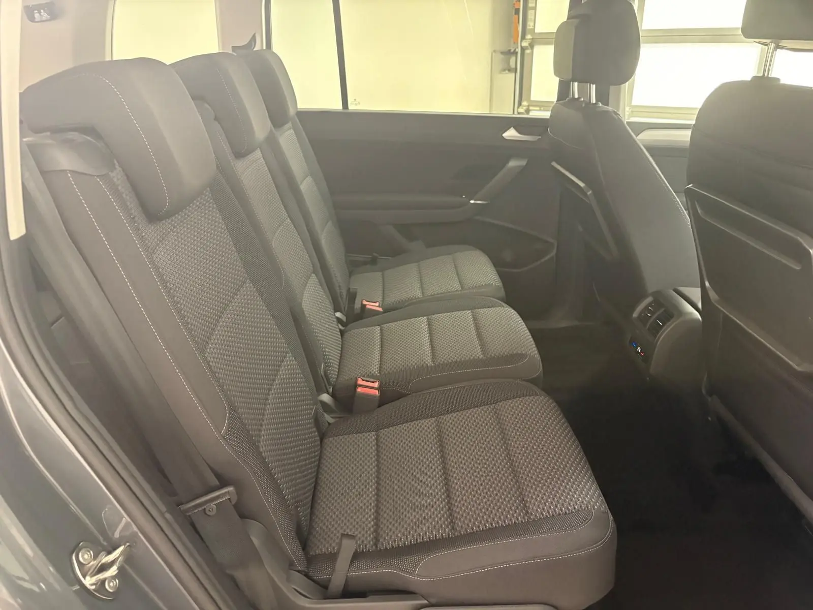 Vue latérale des sièges arrière en tissu gris du Volkswagen Touran 2025, avec appuie-têtes et ceintures visibles.