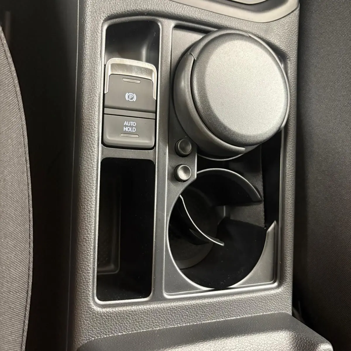 Gros plan sur la console centrale noire du Volkswagen Touran 2025, avec bouton frein à main électrique et porte-gobelet.