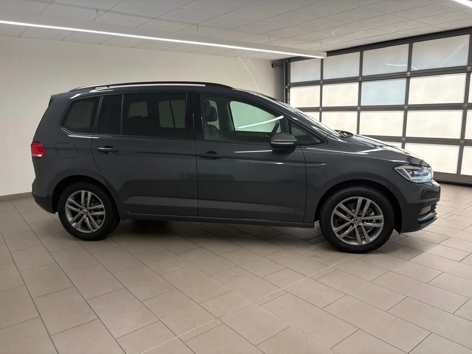 Vue de profil côté gauche du Volkswagen Touran 2025 gris dauphin, soulignant ses lignes épurées et jantes alliage 17 pouces.