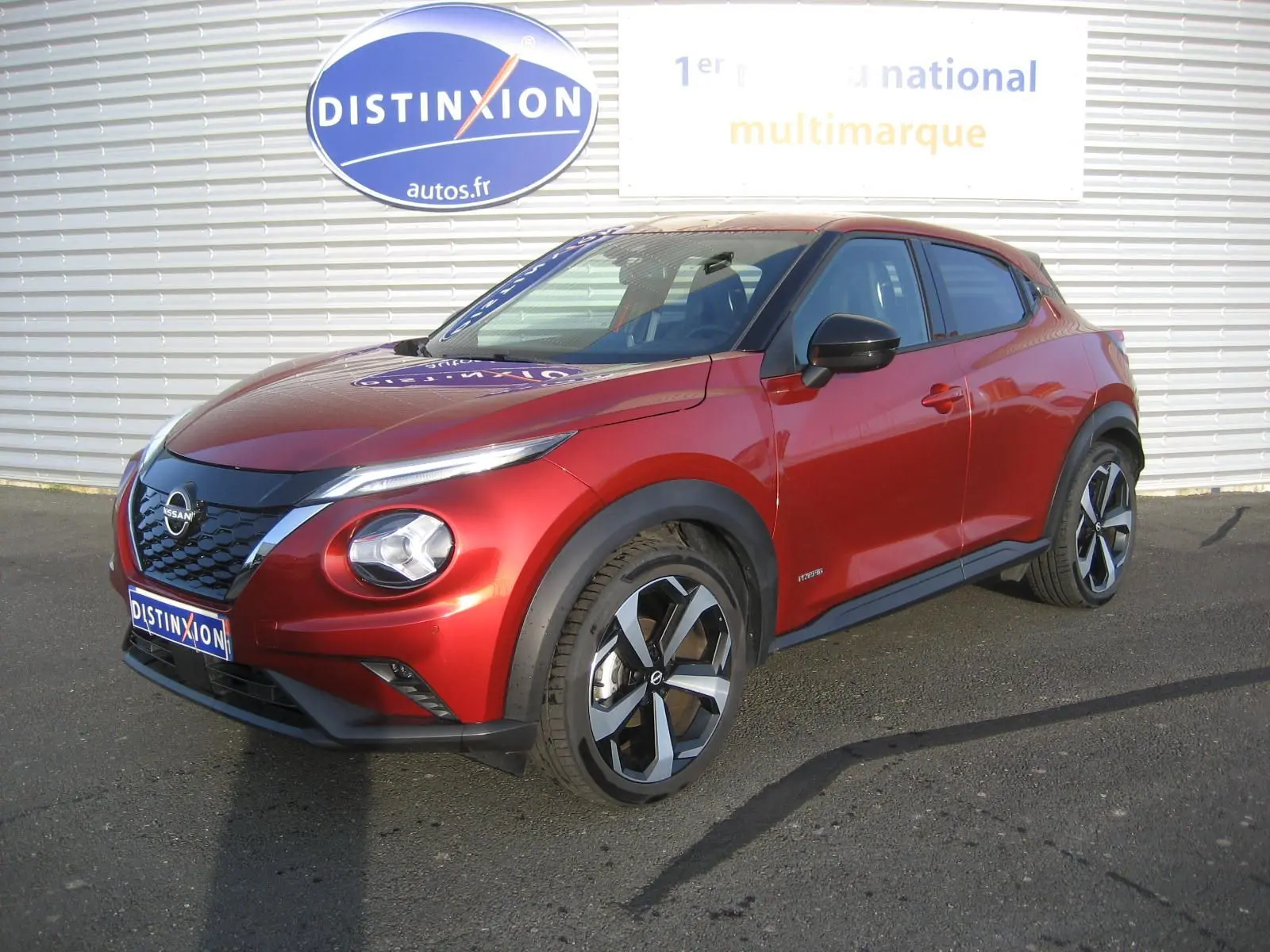 Nissan Juke 1.6 Hybrid 143 Tekna rouge en 3/4 avant droit avec jantes bi-ton et calandre noire brillante.