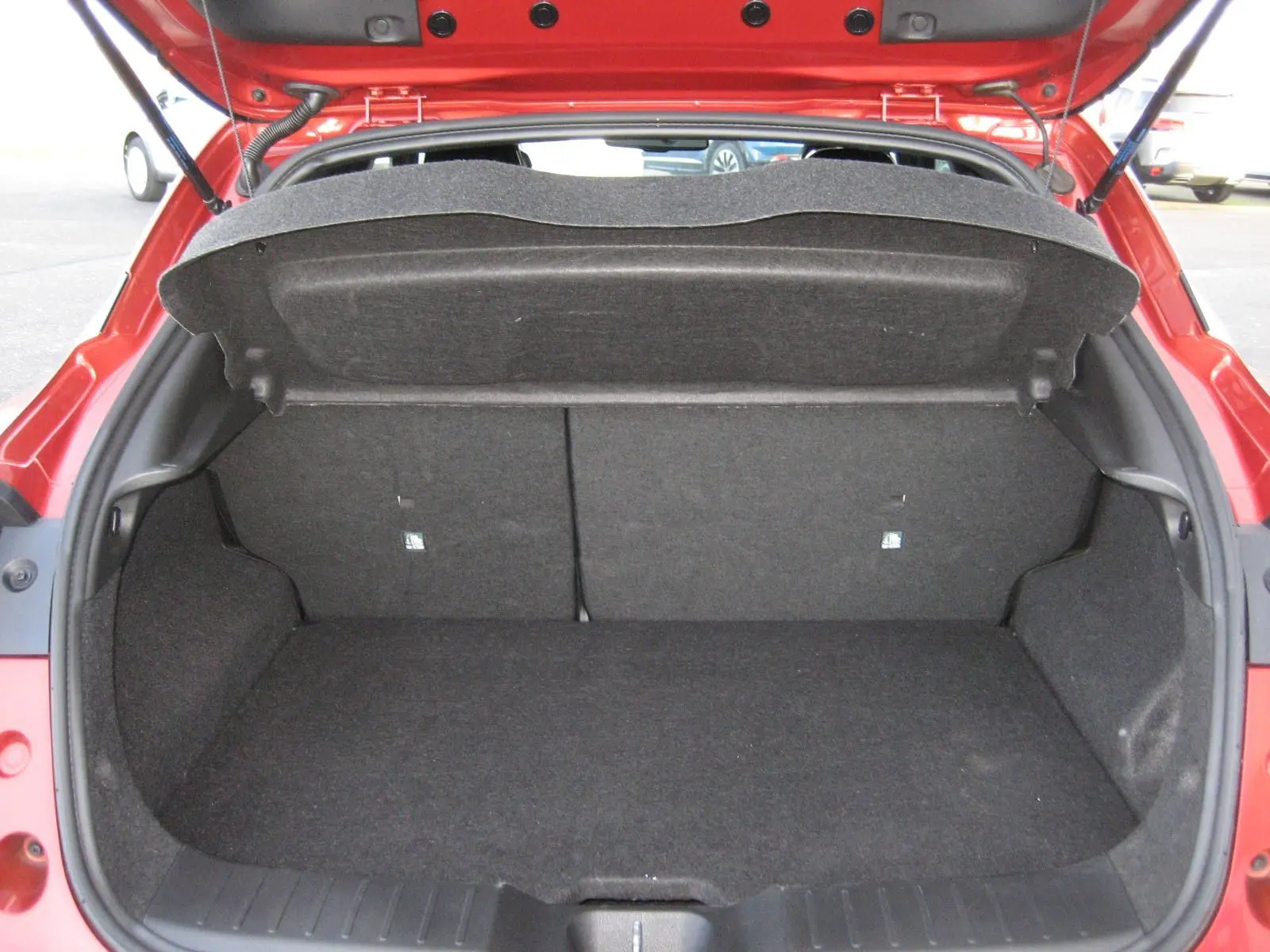 Coffre ouvert vu de l'arrière d'un Nissan Juke 1.6 Hybrid 143 Tekna rouge, montrant un espace de chargement vide et propre.