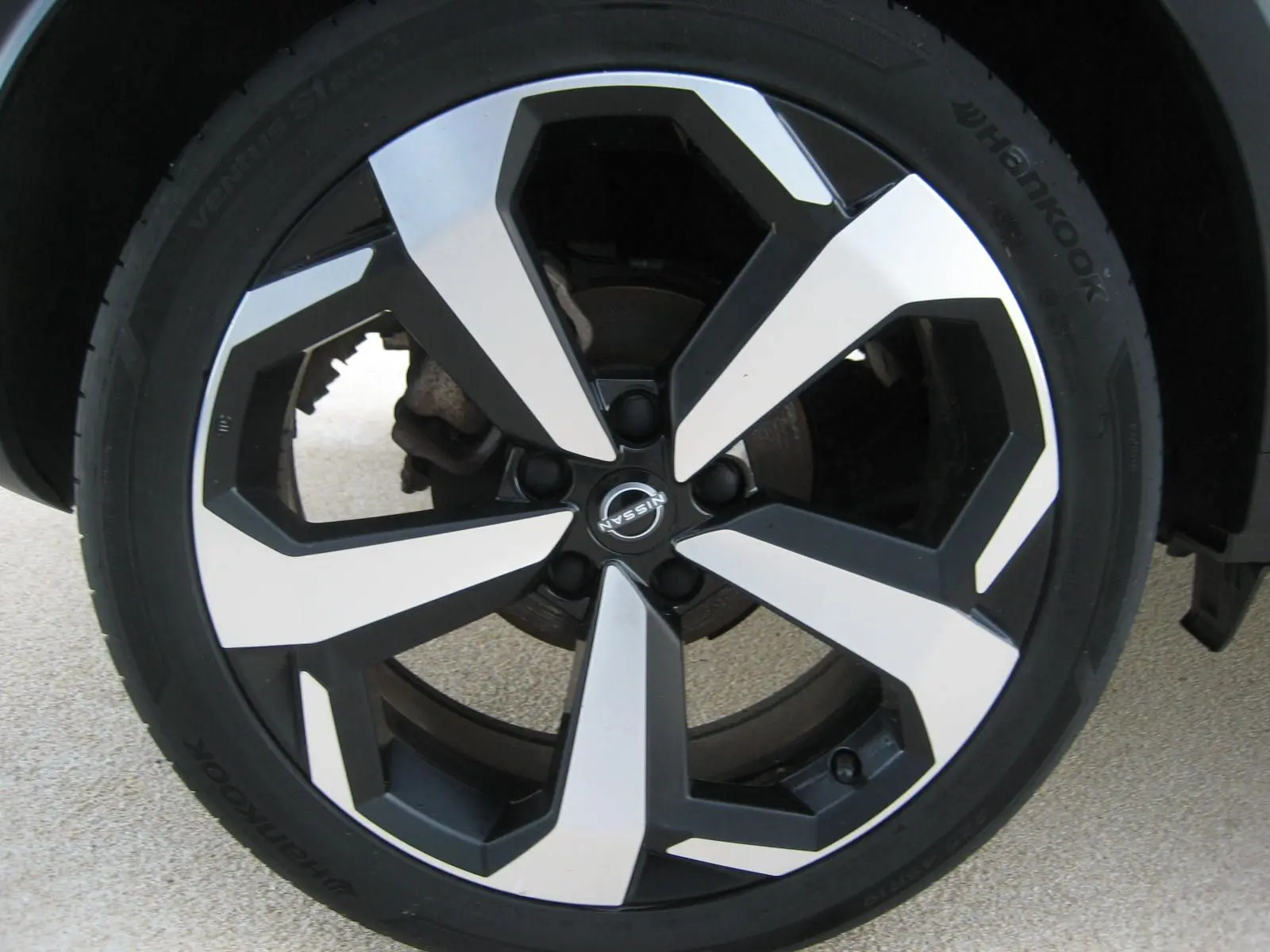 Gros plan sur la jante bi-ton noire et argentée d’un Nissan Juke rouge 2024, mettant en valeur le logo central Nissan.