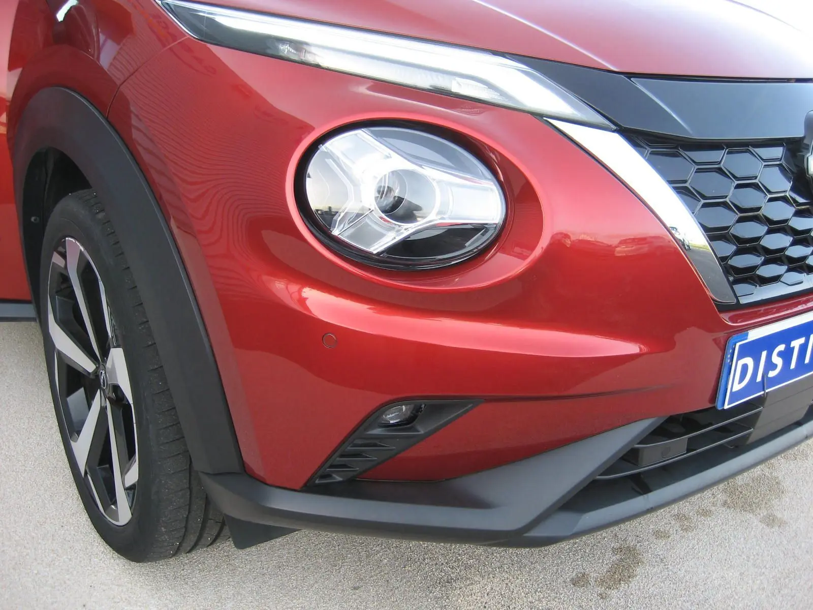 Gros plan sur l’avant droit du Nissan Juke 1.6 Hybrid rouge 2024, mettant en valeur le phare rond et la calandre noire.
