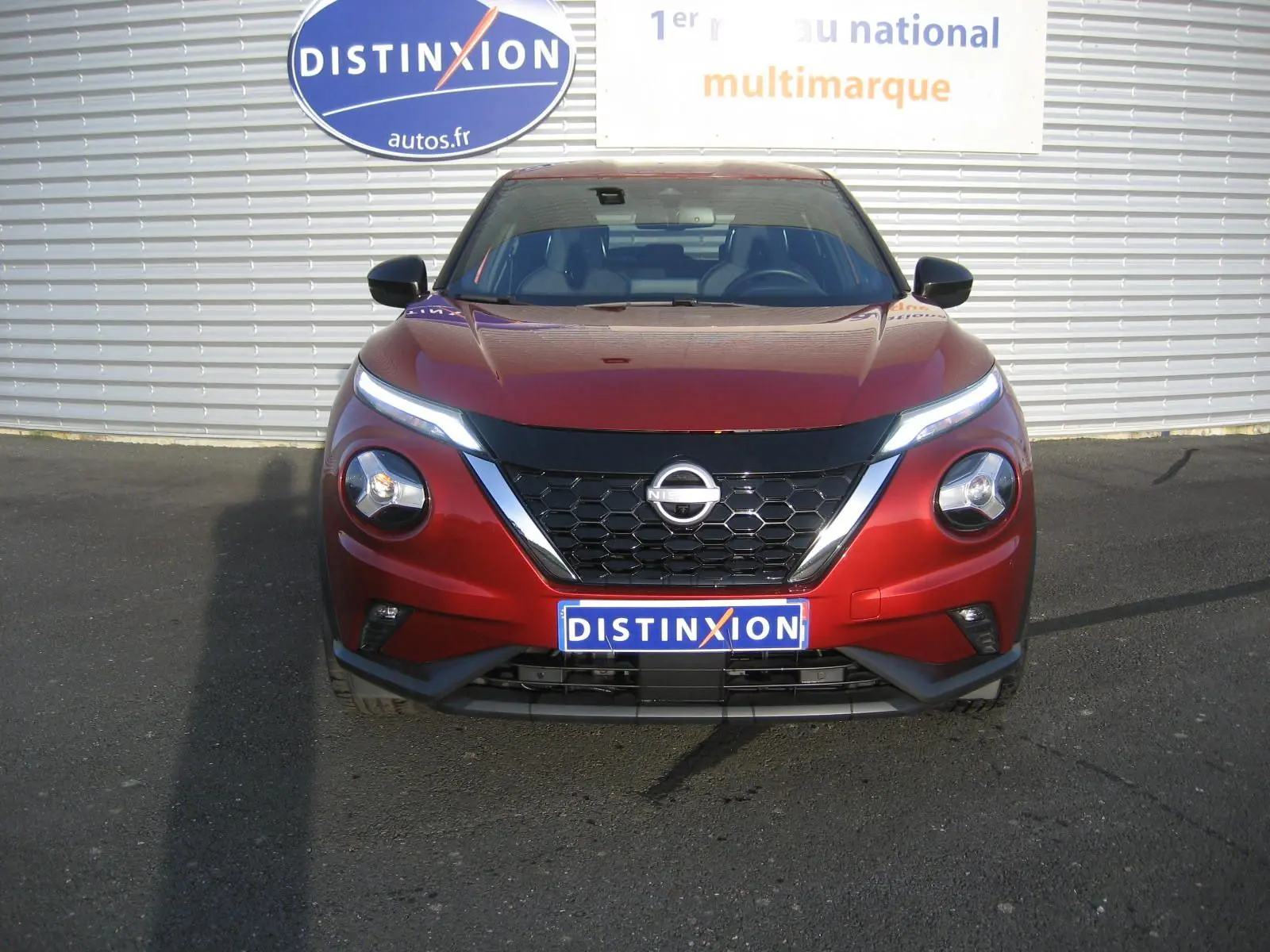Vue frontale d'un Nissan Juke 1.6 Hybrid 143 Tekna rouge, avec calandre noire et phares LED distinctifs allumés.