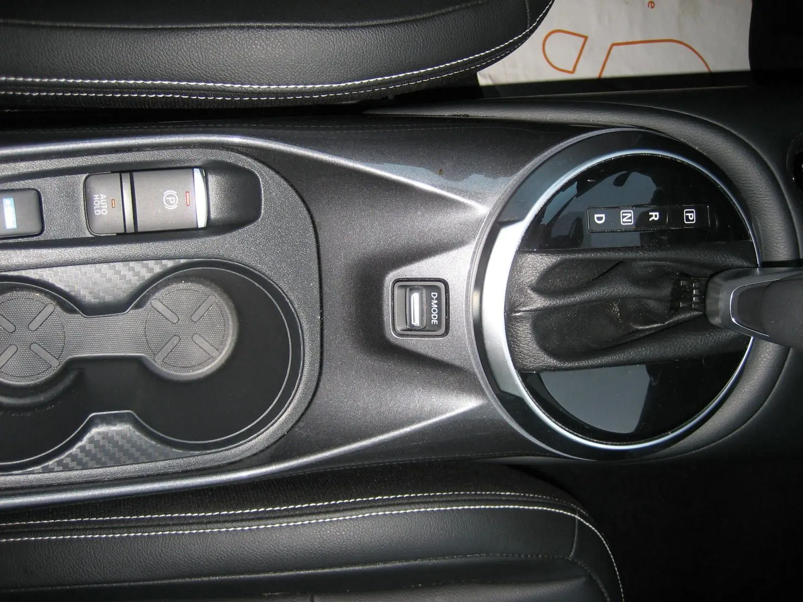 Vue plongeante sur la console centrale noire du Nissan Juke 1.6 Hybrid 143 Tekna avec levier de vitesse automatique et porte-gobelets.