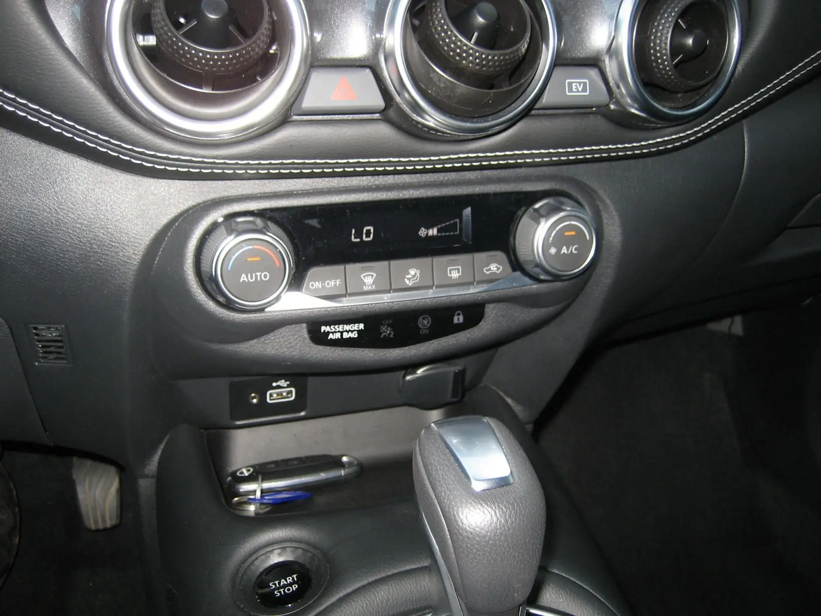 Gros plan sur la console centrale du Nissan Juke rouge 2024, montrant la commande de climatisation et le levier de vitesse automatique.