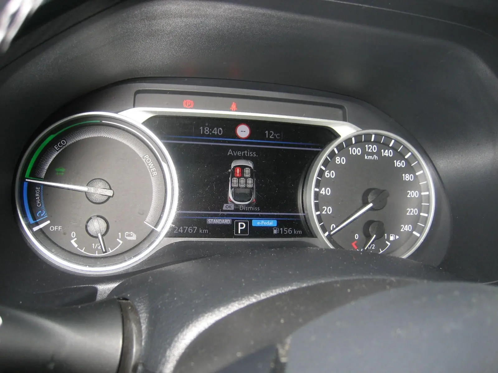 Vue rapprochée du tableau de bord numérique du Nissan Juke 1.6 Hybrid 143 Tekna, affichant l'alerte et la vitesse.