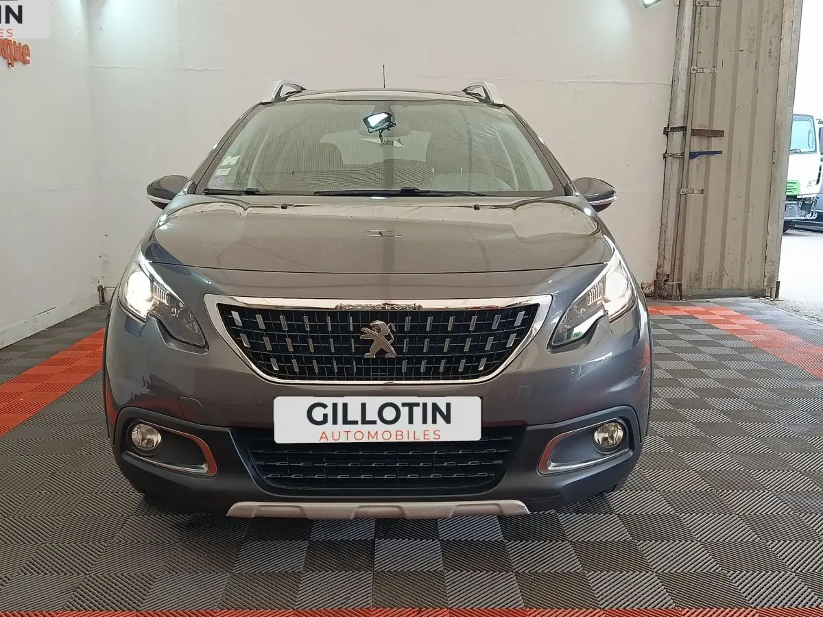 Vue de face d'un Peugeot 2008 gris foncé avec calandre chromée et feux allumés dans un garage.
