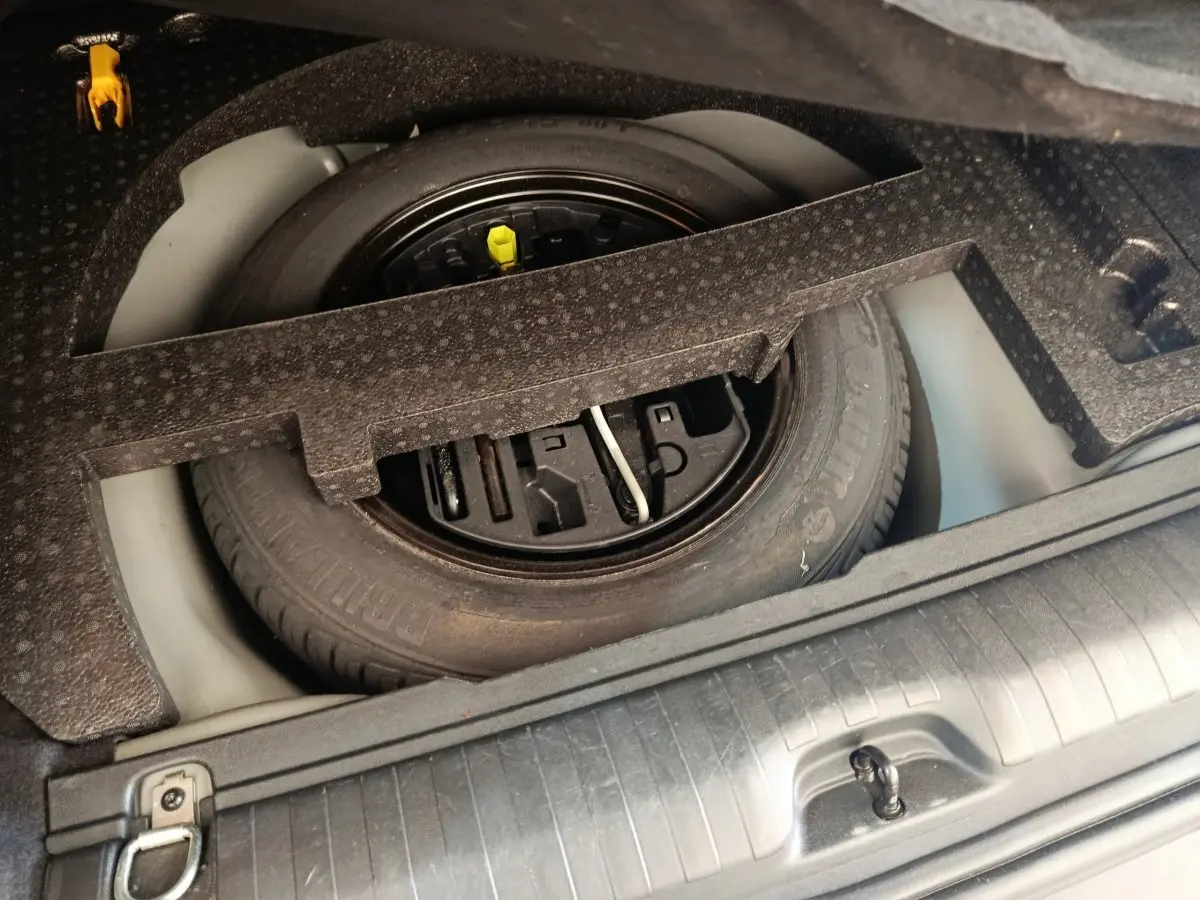 Vue rapprochée de la roue de secours dans le coffre d’un Peugeot 2008 gris foncé, avec outils de changement intégrés.