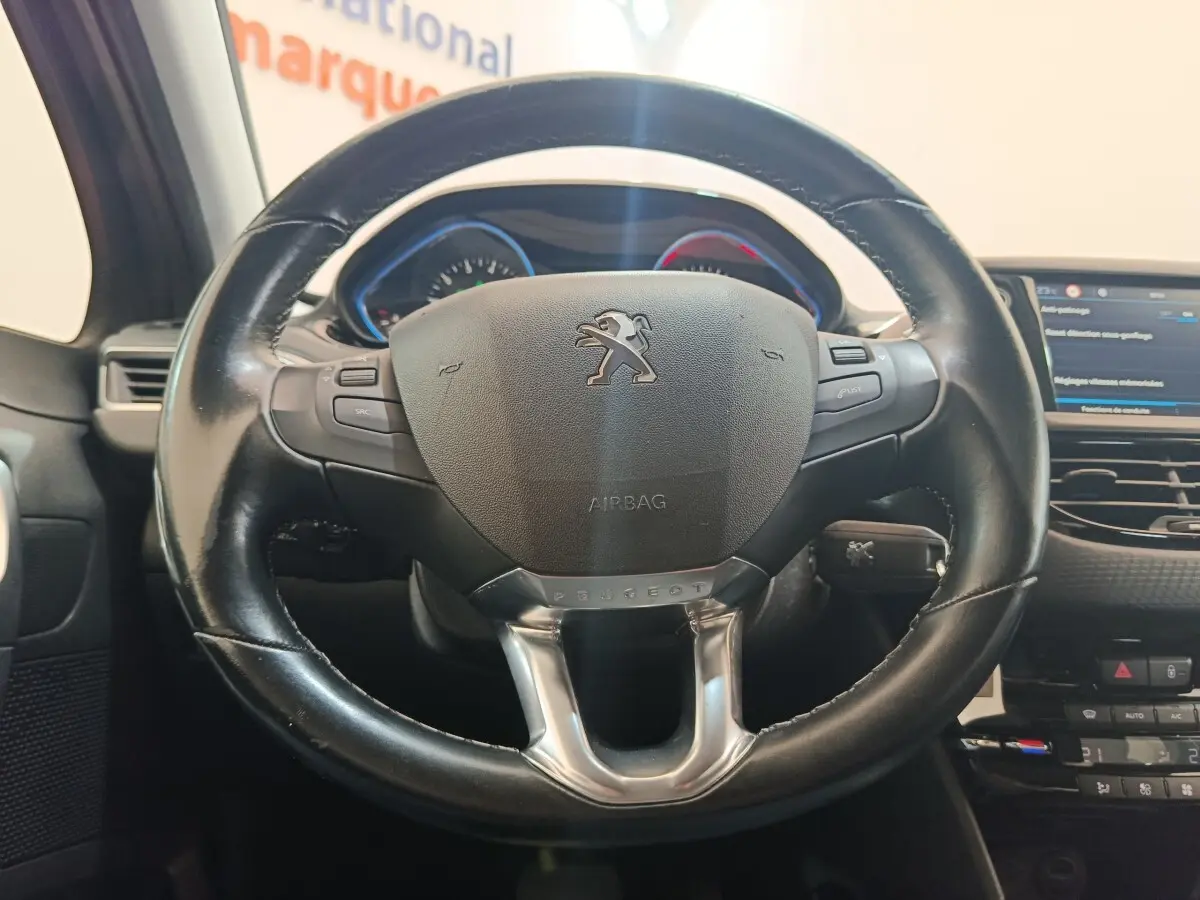 Vue rapprochée du volant cuir noir multifonctions du Peugeot 2008 gris foncé avec tableau de bord et écran tactile visibles.