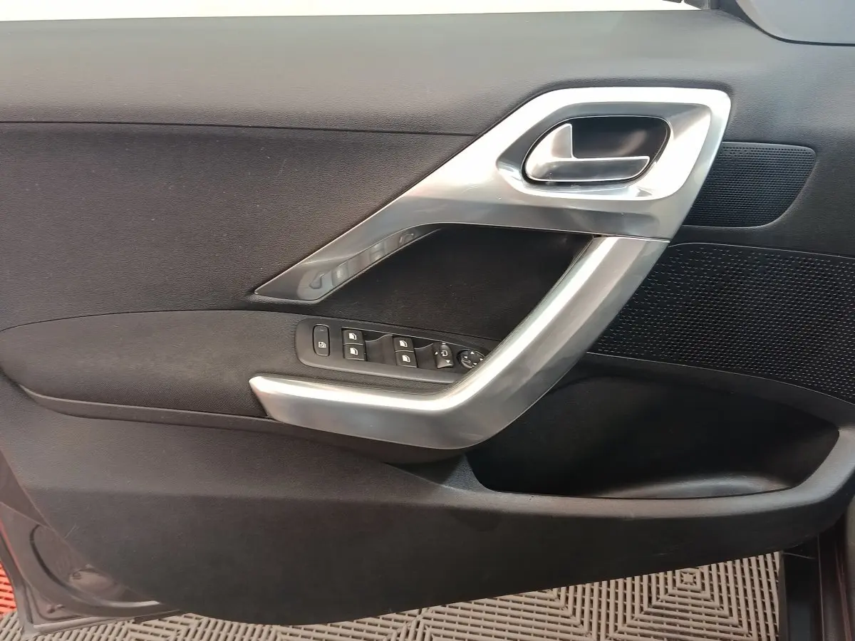 Détail de la porte intérieure côté gauche de Peugeot 2008 gris foncé avec poignée argentée et commandes des vitres.