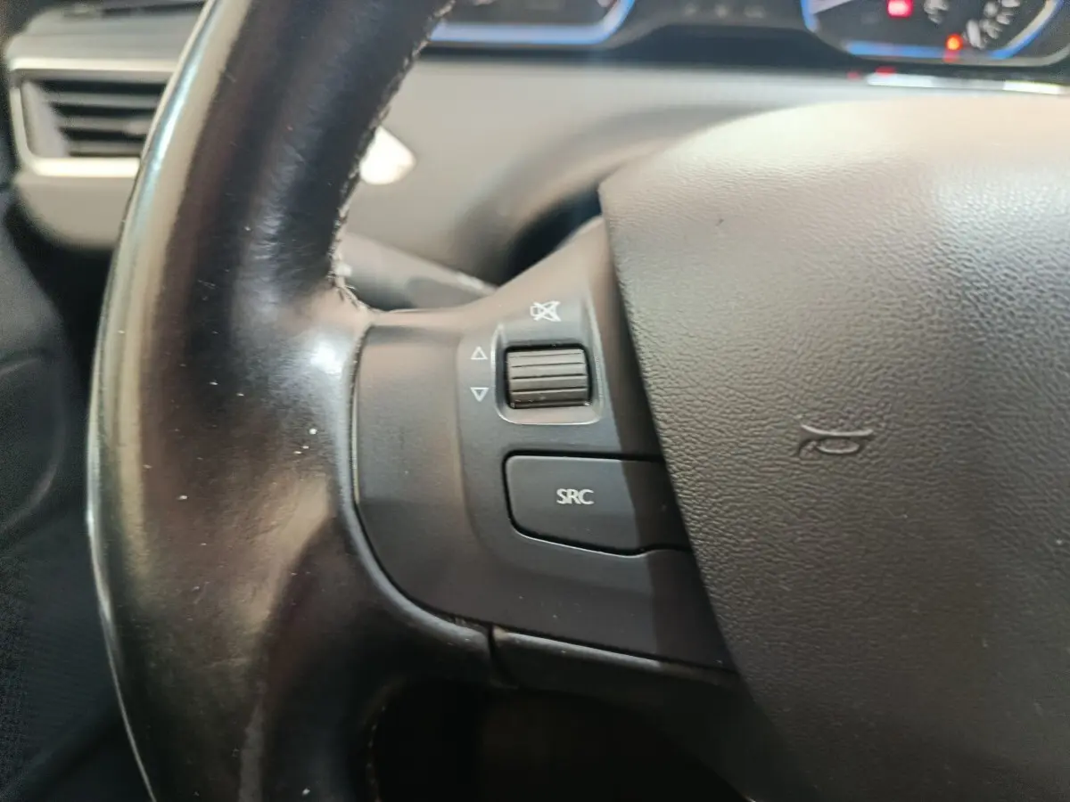 Gros plan sur le volant en cuir noir côté gauche du Peugeot 2008 gris foncé, avec commandes audio intégrées.