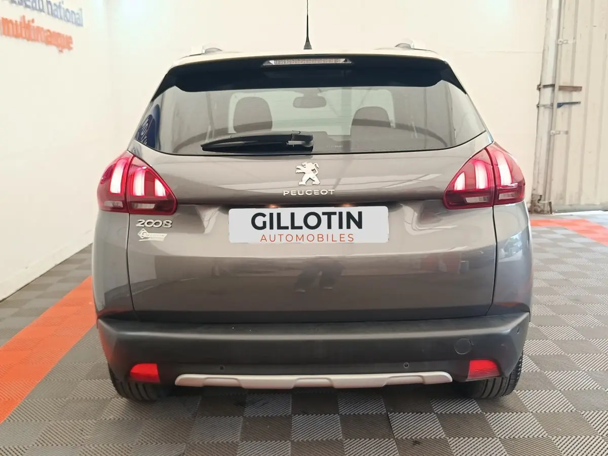 Vue arrière d'un Peugeot 2008 gris foncé avec feux allumés et logo visible dans un showroom.