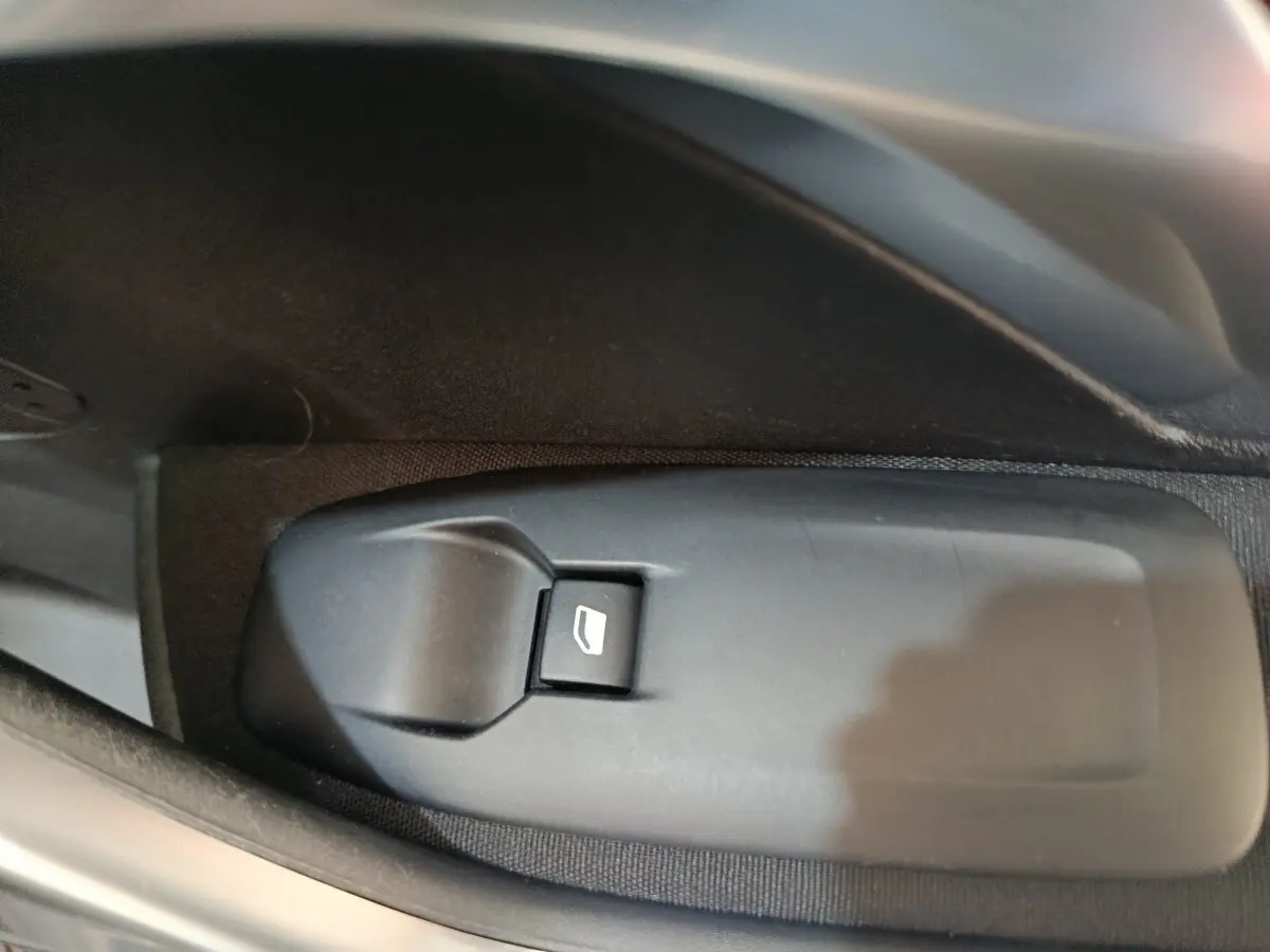 Gros plan sur le bouton de commande de lève-vitre côté conducteur d’un Peugeot 2008 gris foncé de 2019.