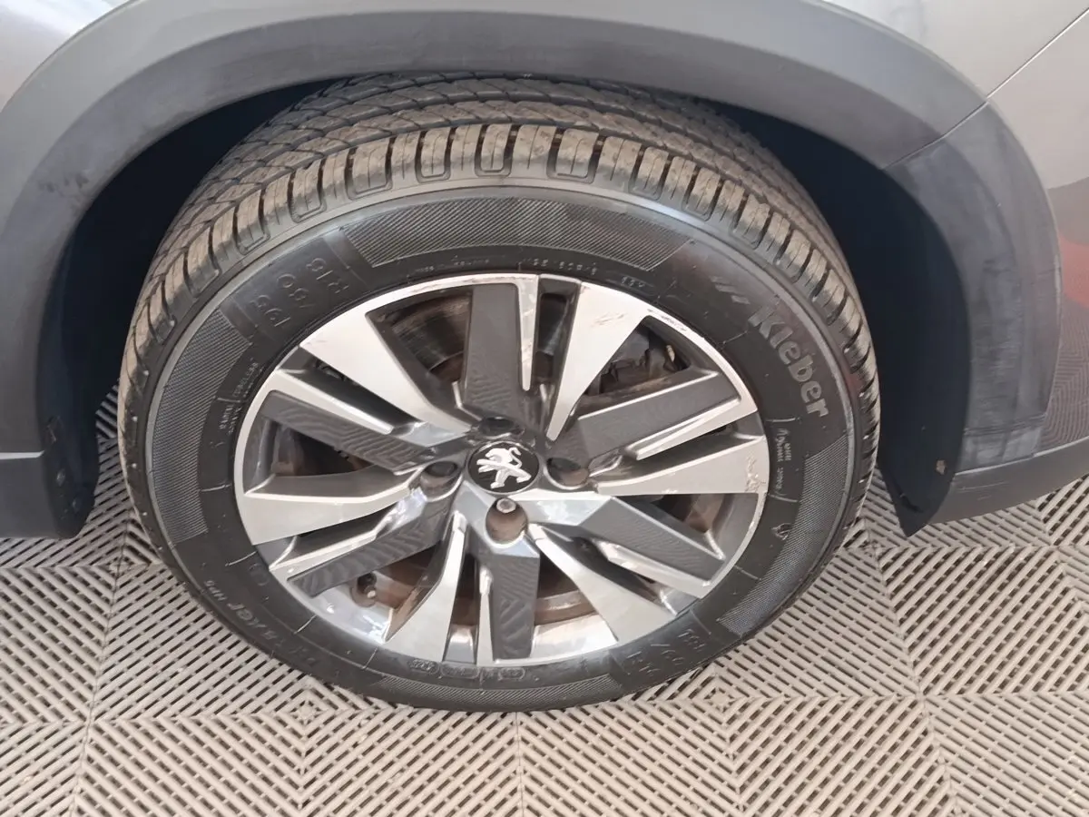 Gros plan sur la roue avant droite d’un Peugeot 2008 gris foncé, avec jante alliage et logo lion au centre.