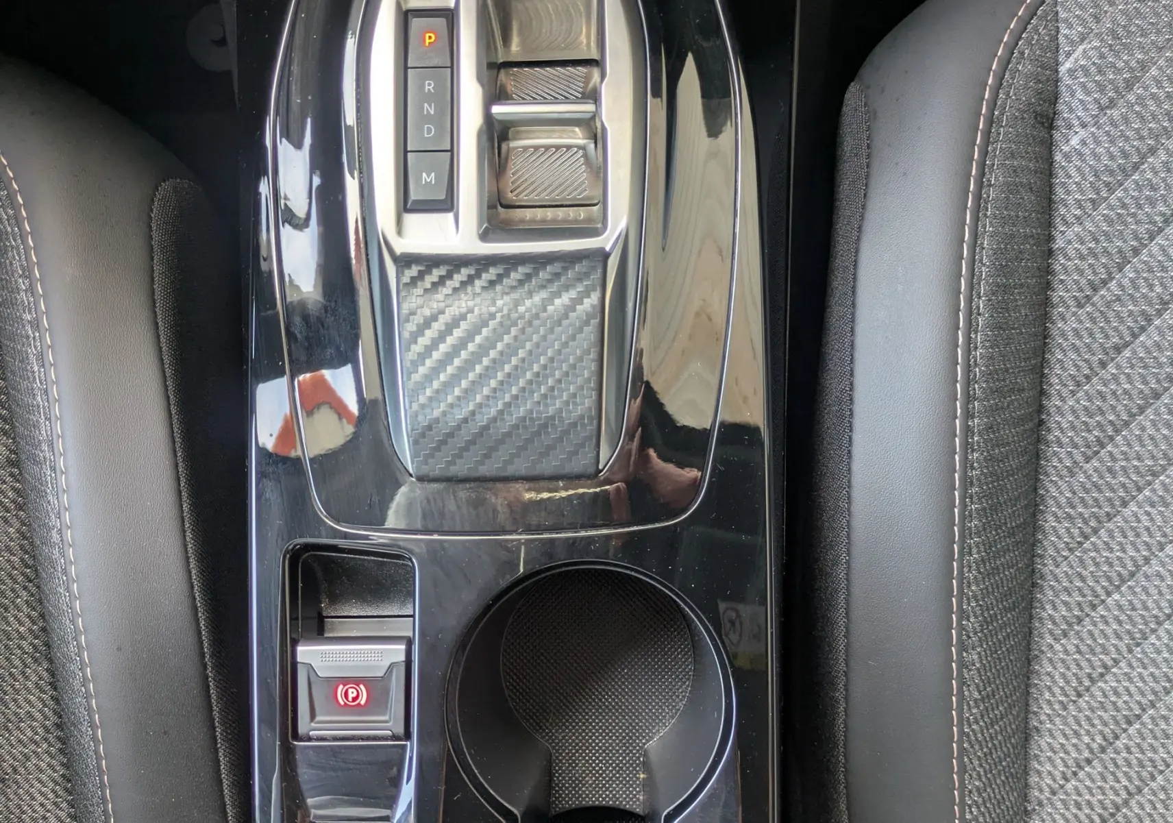 Vue plongeante sur la console centrale noire brillante du Peugeot 2008 Hybrid 145, avec levier de vitesses et sellerie tissu gris.