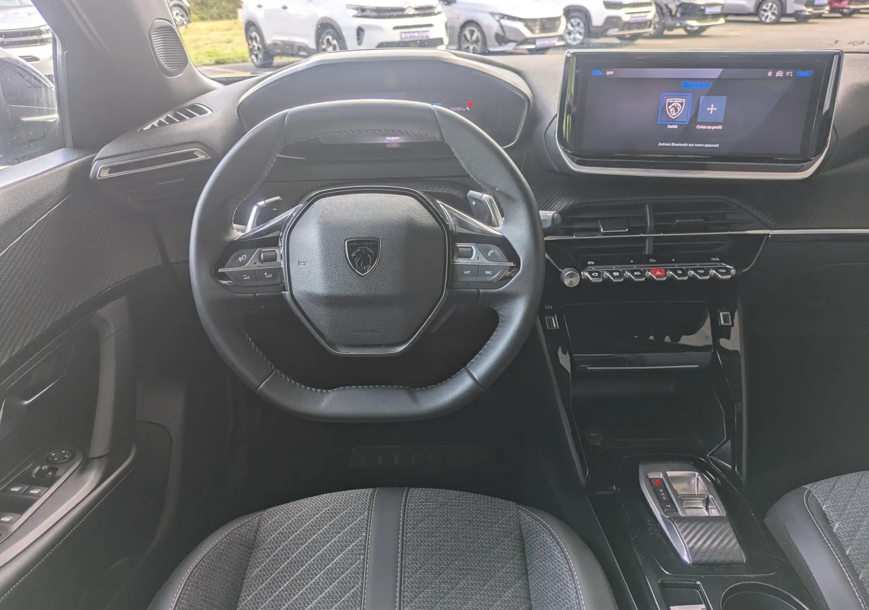 Vue intérieure centrée sur le volant compact et le tableau de bord numérique du Peugeot 2008 Hybrid 145, sellerie tissu grise.