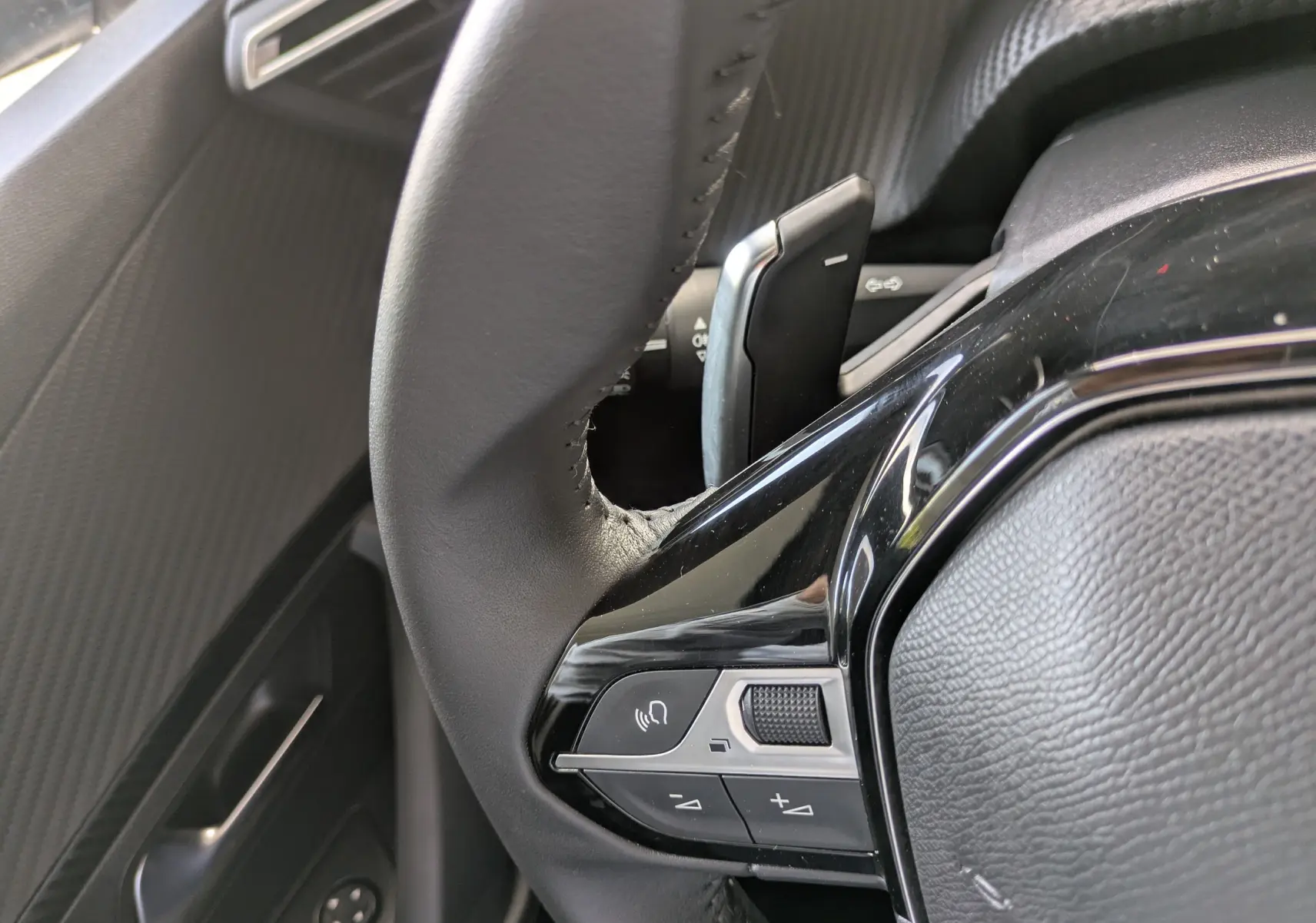 Gros plan sur les commandes au volant côté gauche du Peugeot 2008 Hybrid 145, avec finition noire brillante.
