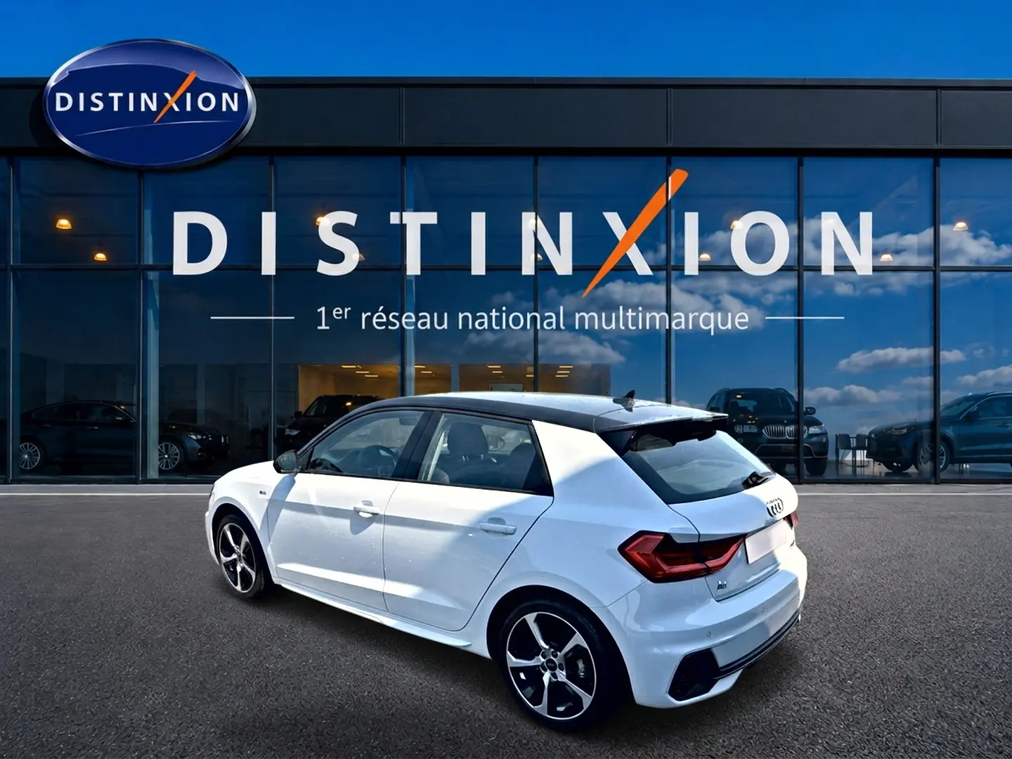 Audi A1 Sportback blanc toit noir en 3/4 arrière droit, avec jantes alu et becquet arrière visible devant showroom Distinxion.