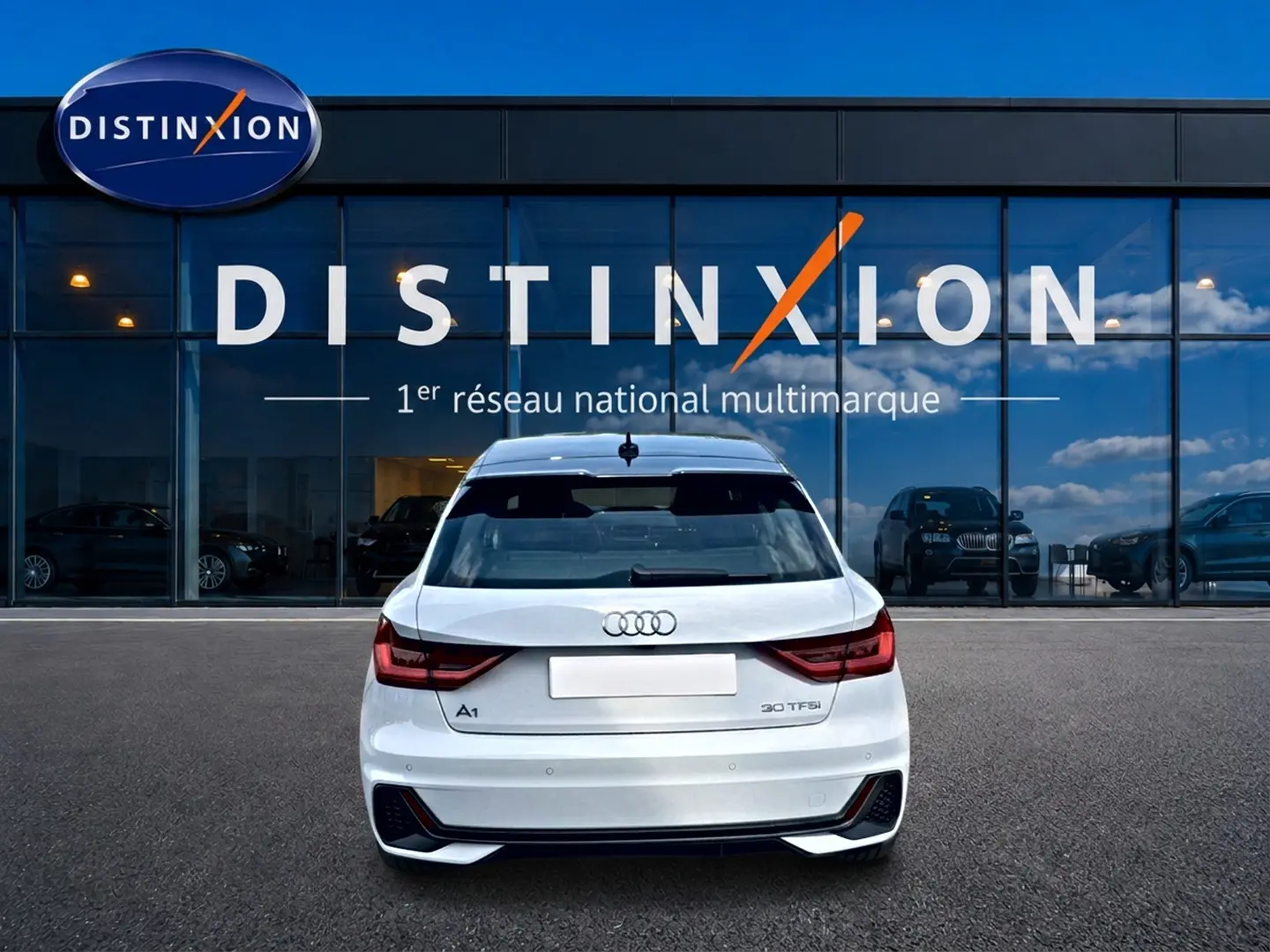 Vue arrière d'une Audi A1 Sportback blanc et noir, avec feux LED et becquet arrière, stationnée devant une vitrine Distinxion.