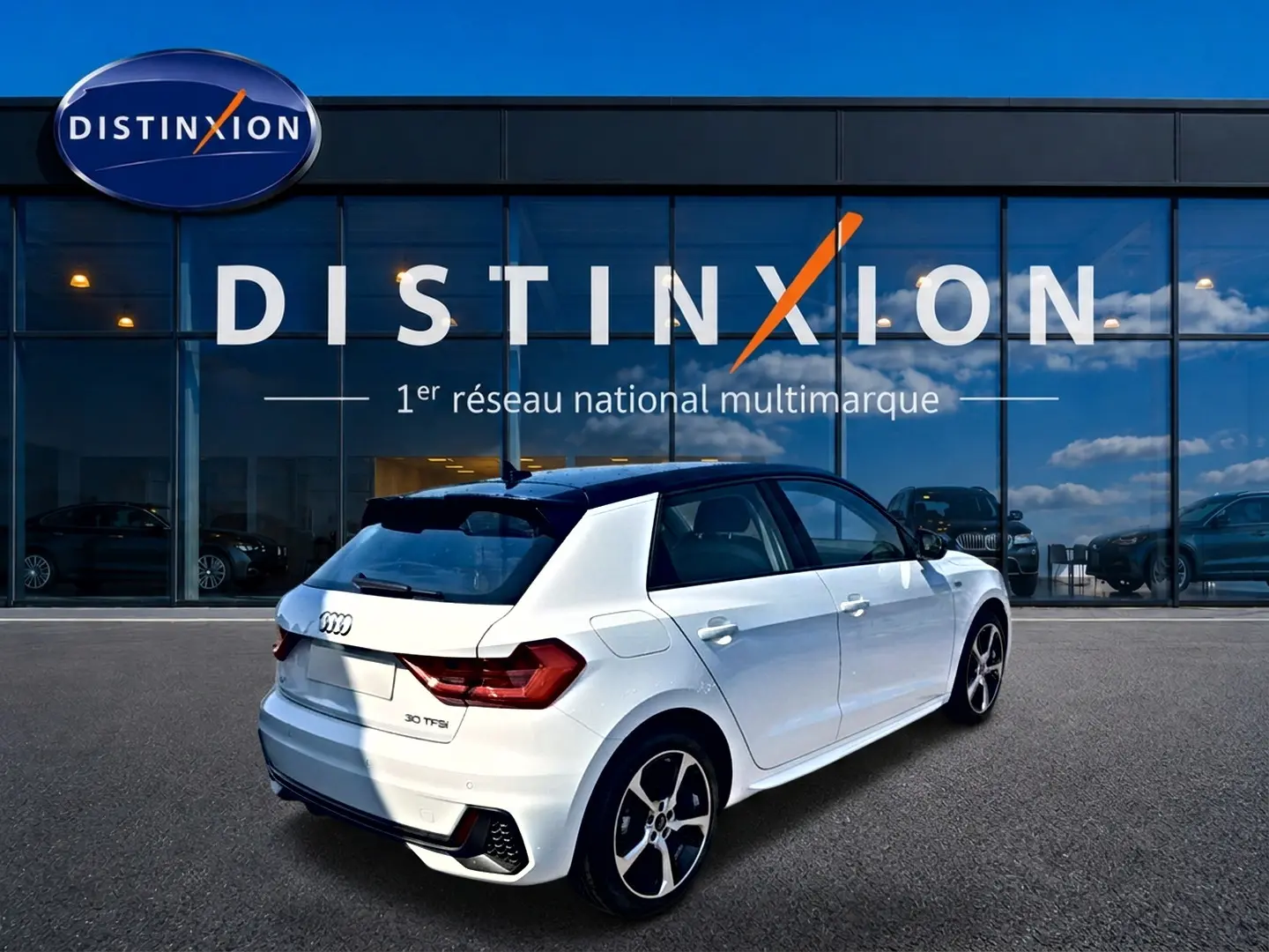 Audi A1 Sportback blanc et noir en 3/4 arrière droit, avec jantes alu et becquet arrière visible devant un showroom Distinxion.