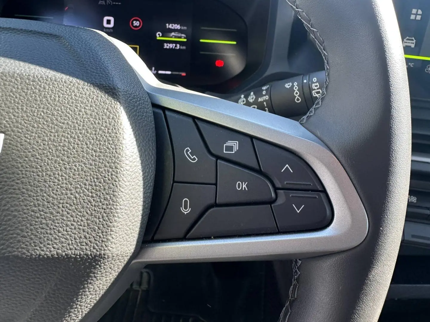 Gros plan sur le volant multifonction noir du Dacia Duster 2025, avec commandes vocales et téléphone côté droit.