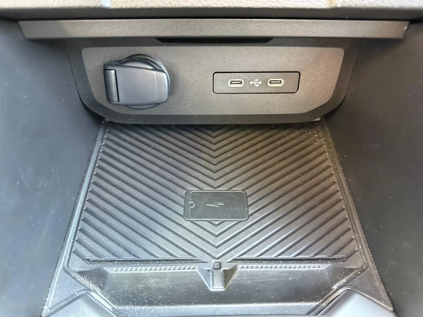 Gros plan sur la zone de recharge avec ports USB-C et prise 12V dans le compartiment central noir du Dacia Duster.