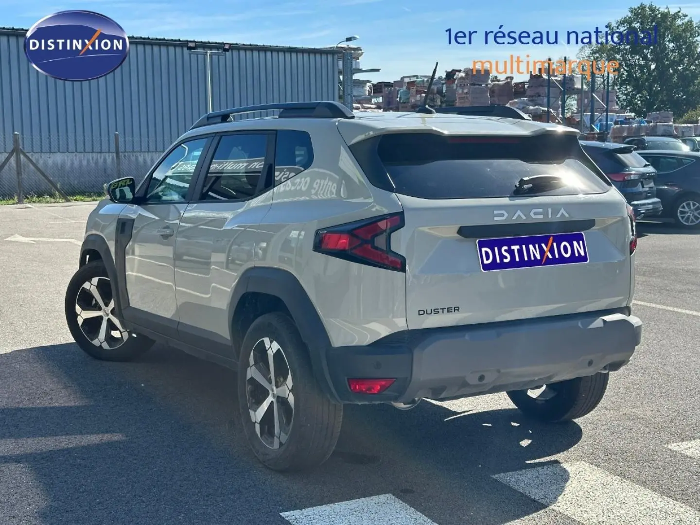 Vue 3/4 arrière droite du Dacia Duster 2025 couleur Sandstone avec barres de toit et jantes alliage.