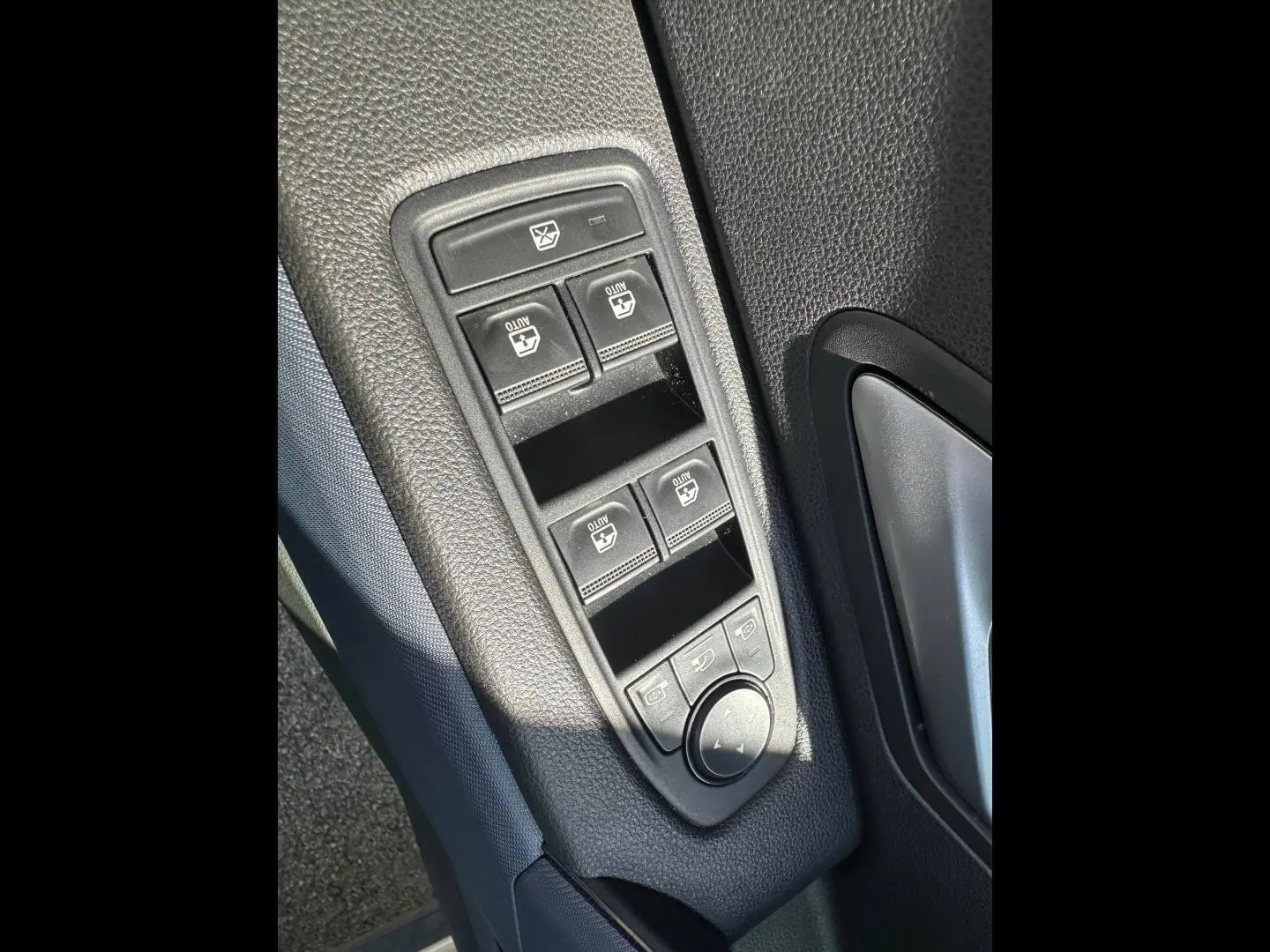 Gros plan sur les commandes des vitres électriques et rétroviseurs côté conducteur du Dacia Duster 2025 couleur Sandstone.