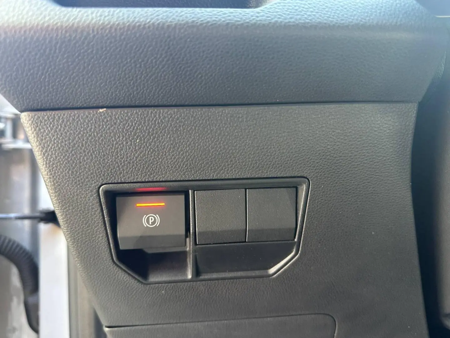 Bouton de frein de stationnement électronique allumé sur tableau de bord noir du Dacia Duster 2025.