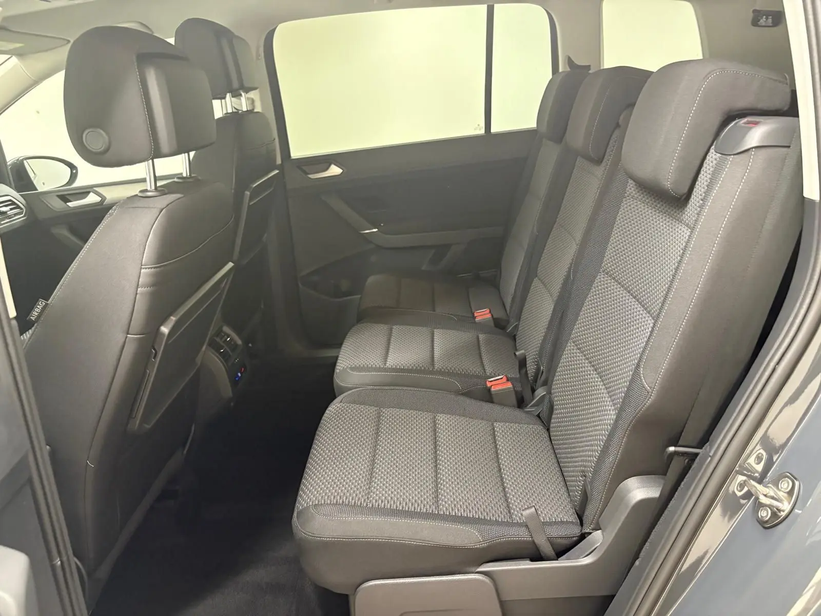 Vue latérale droite de l'habitacle arrière du Volkswagen Touran gris Dauphin 2025, montrant les trois sièges en tissu gris avec appuie-têtes.