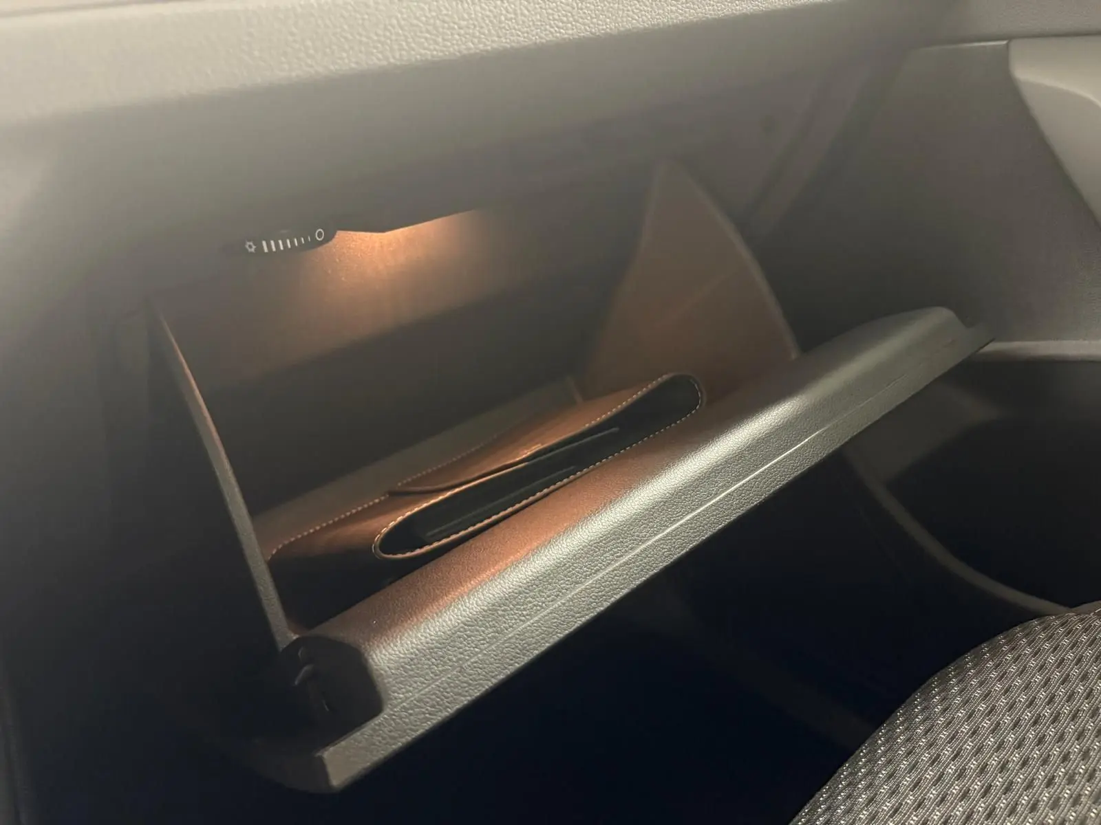 Gant de rangement ouvert éclairé dans l'habitacle du Volkswagen Touran gris Dauphin, côté passager.