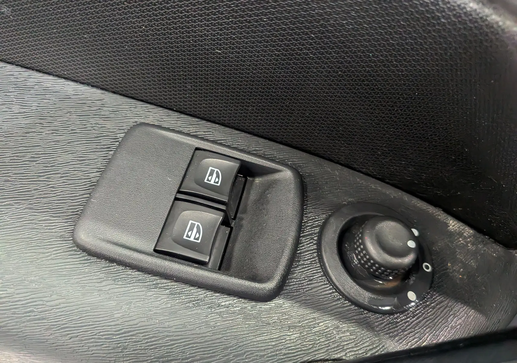 Gros plan sur les commandes électriques des vitres et le réglage des rétroviseurs sur la porte intérieure noire d’un Renault Kangoo Express.