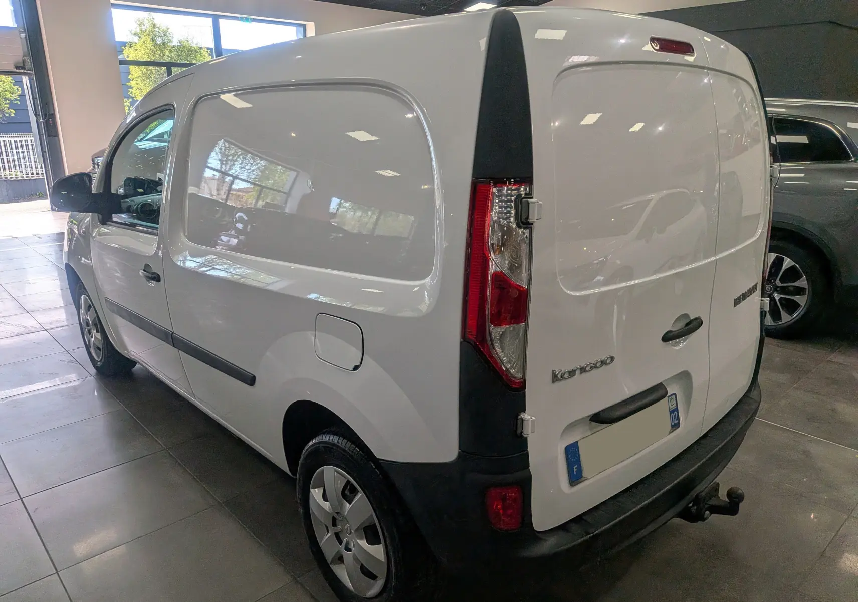 Vue 3/4 arrière droite d’un Renault Kangoo Express blanc Minéral, utilitaire compact avec hayon arrière fermé en intérieur showroom.