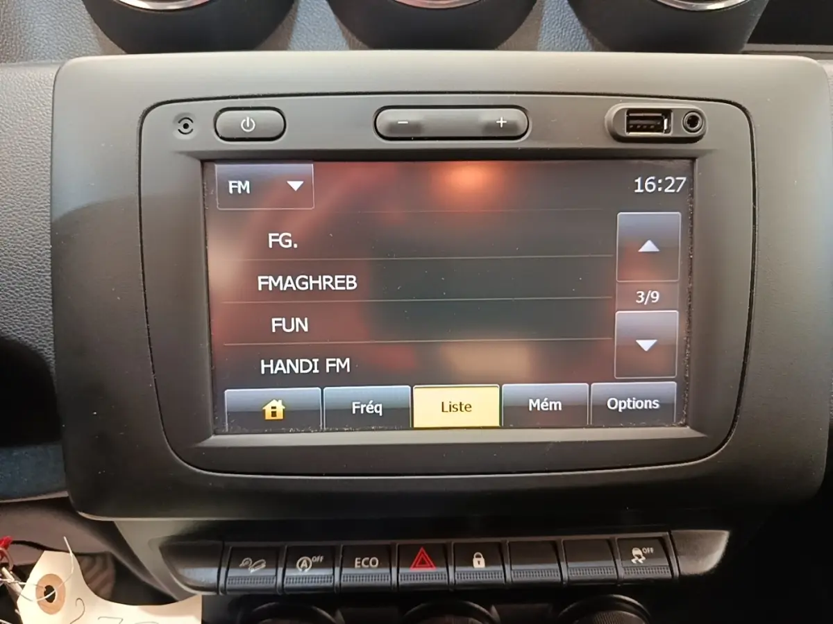 Écran tactile central du tableau de bord du Dacia Duster blanc, affichant les stations radio FM.