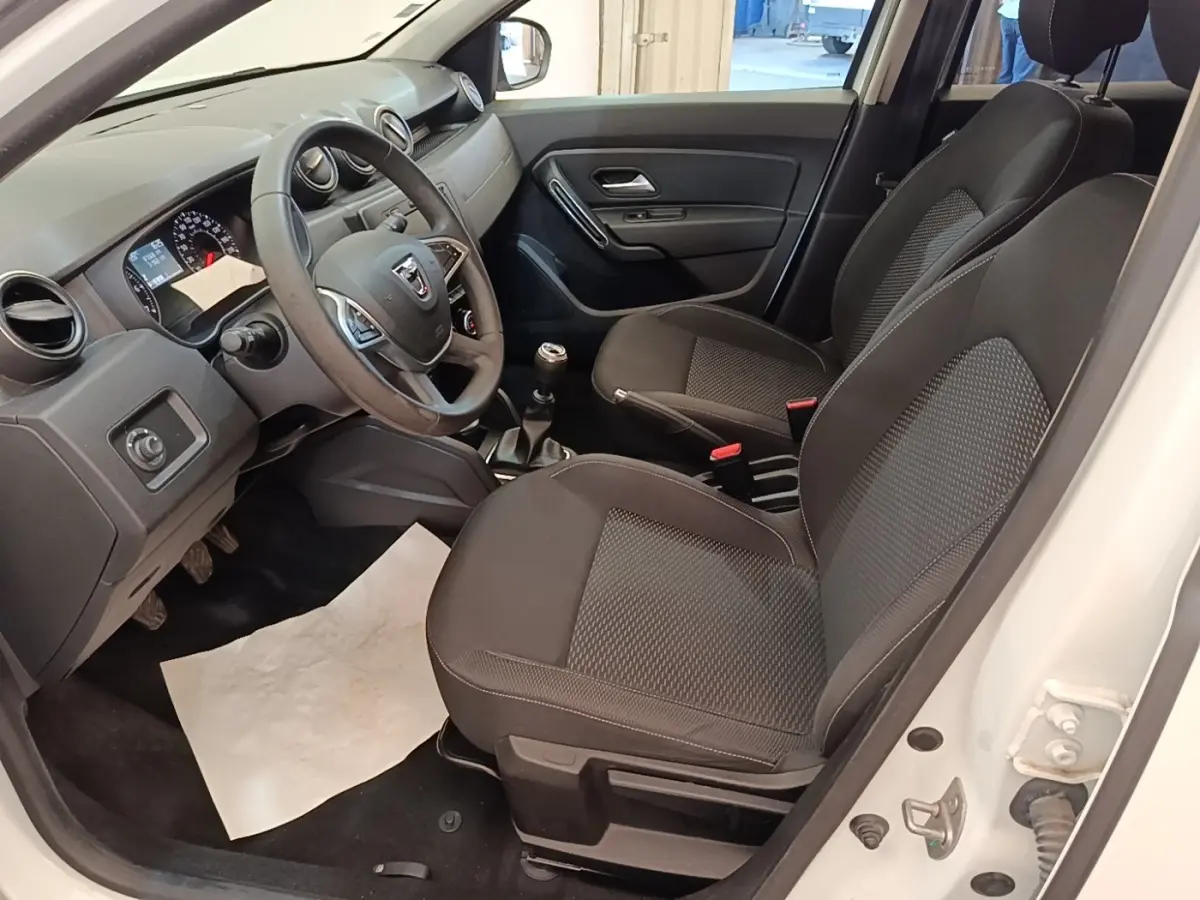Vue intérieure côté conducteur du Dacia Duster blanc 2021, volant multifonctions cuir synthétique et sièges tissu noirs.