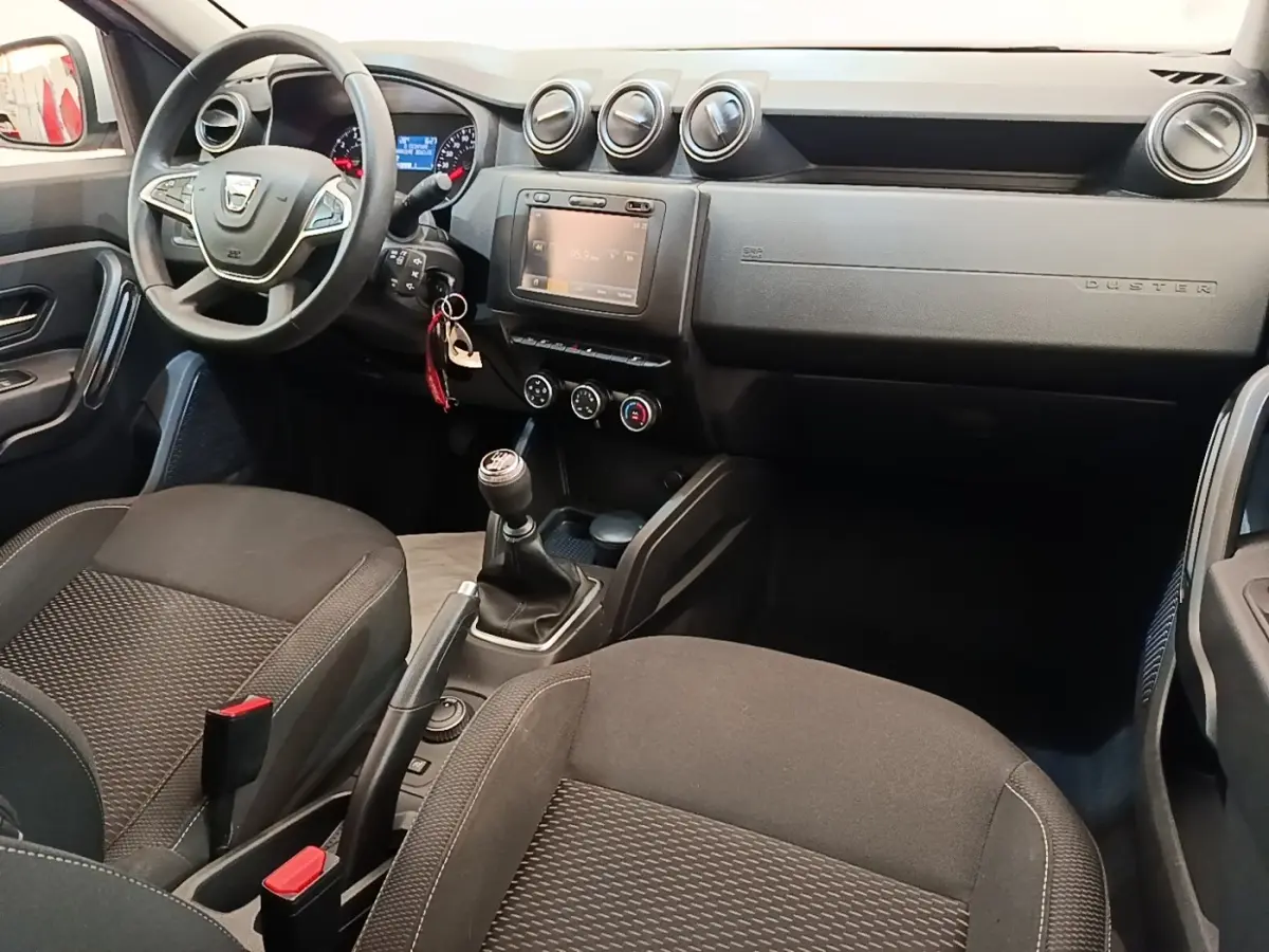 Vue intérieure avant droite du Dacia Duster 2021, tableau de bord noir avec écran tactile et volant multifonctions cuir synthétique.
